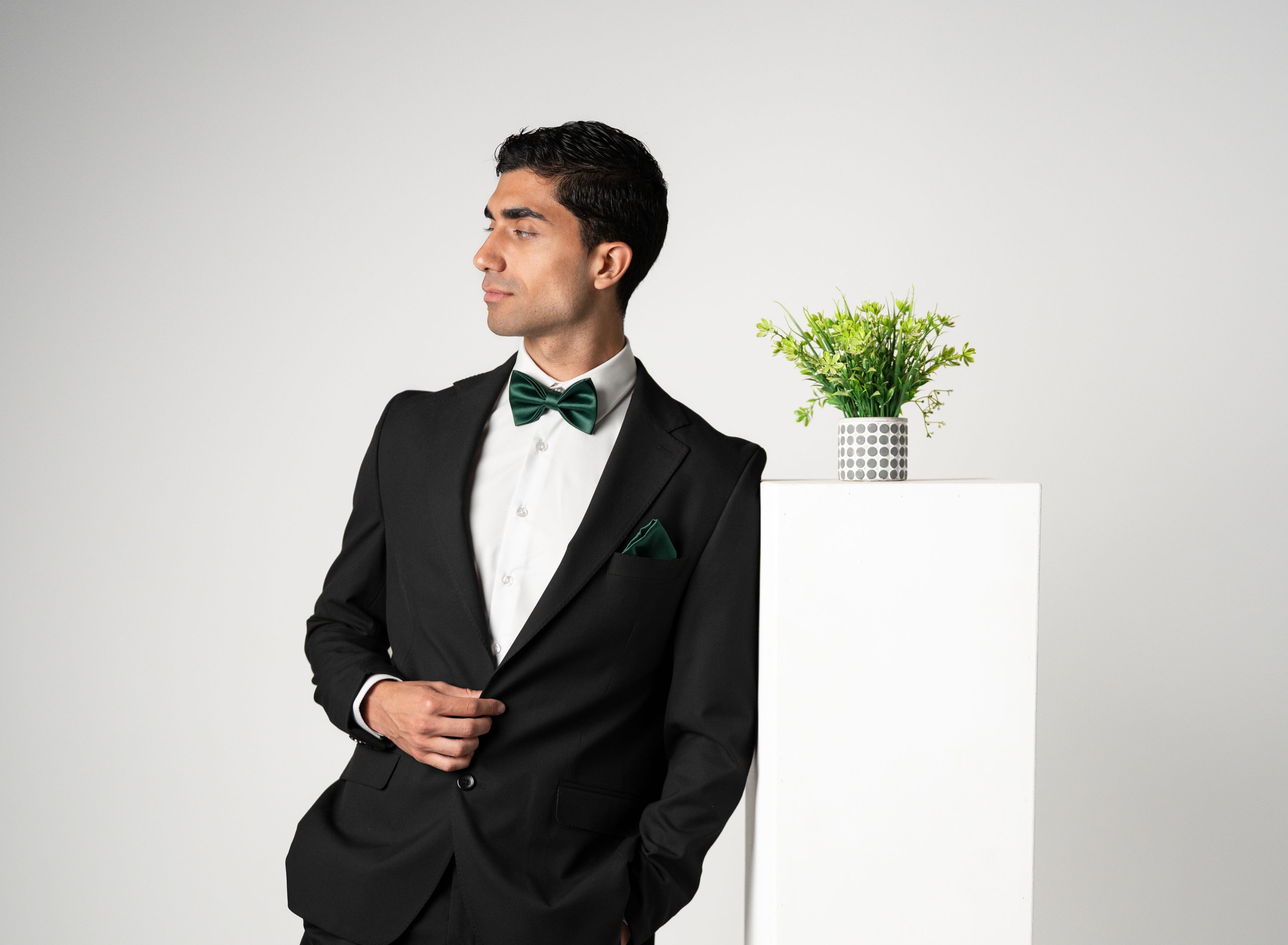 Man in a black tuxedo with green bow tie standing against a white background