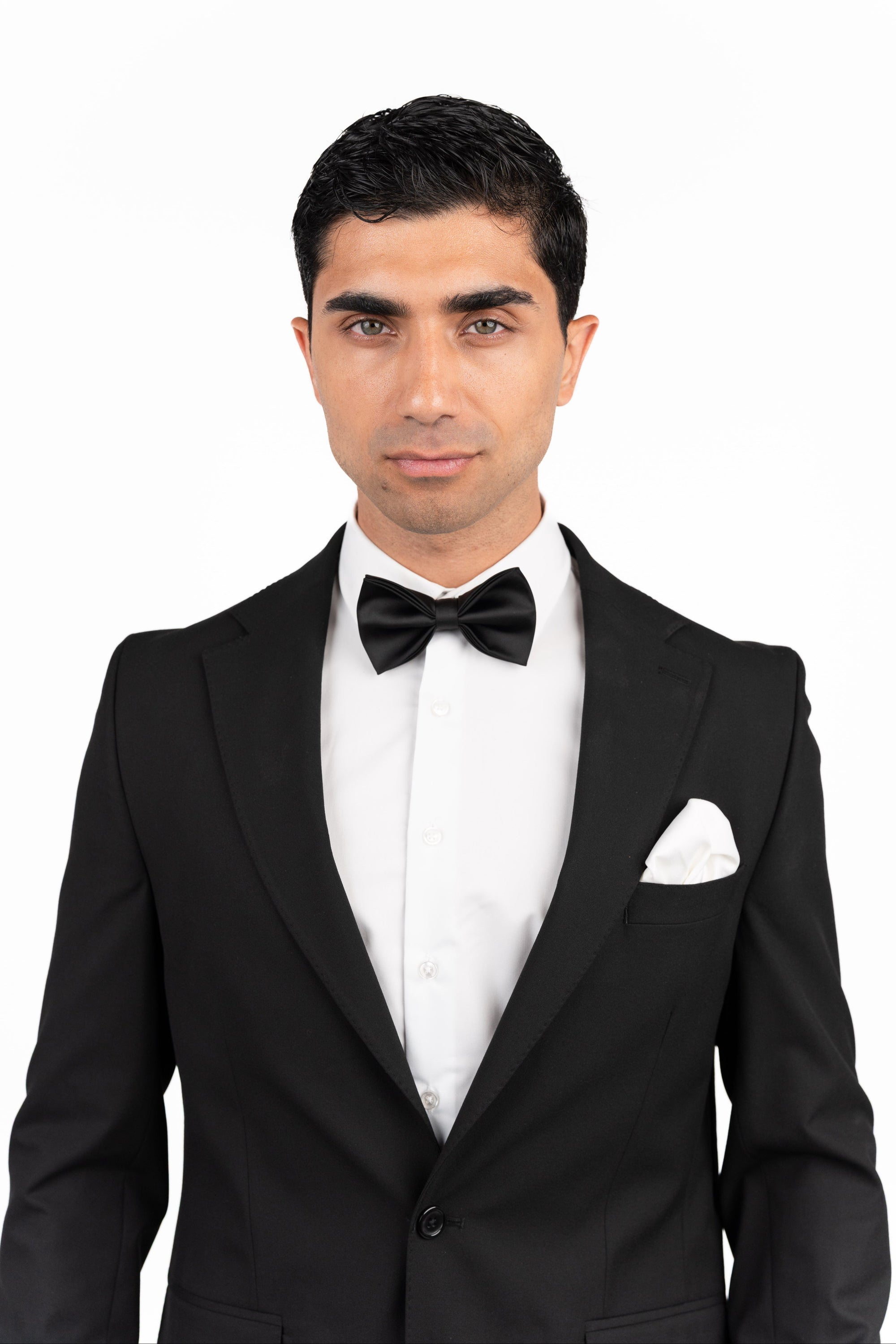 Man wearing a black tuxedo with a bow tie on a white background