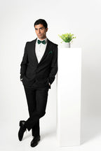 Man in a black suit with a green bow tie standing against a white background