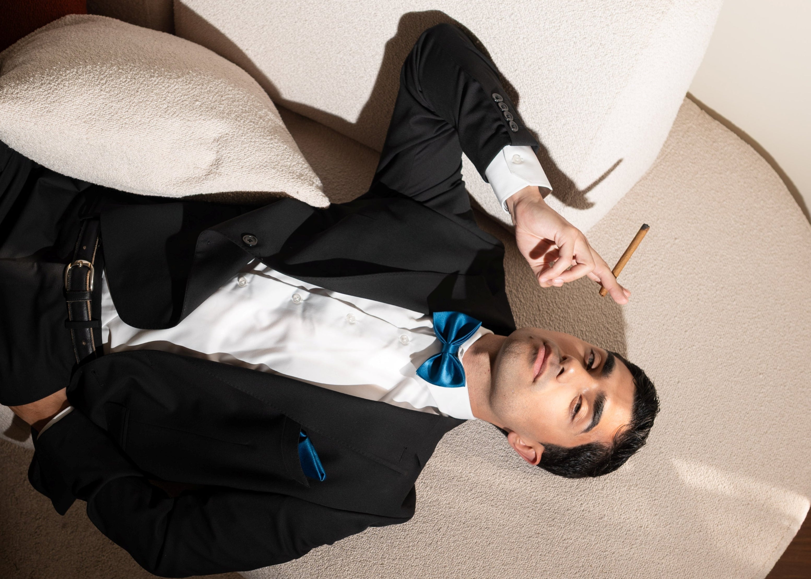 Man in a suit with a blue bow tie lying on a white surface
