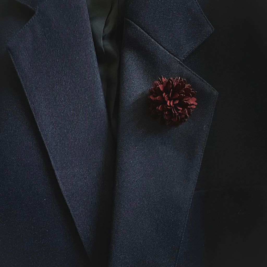Dark blue blazer with a pine cone-shaped pin on a black background