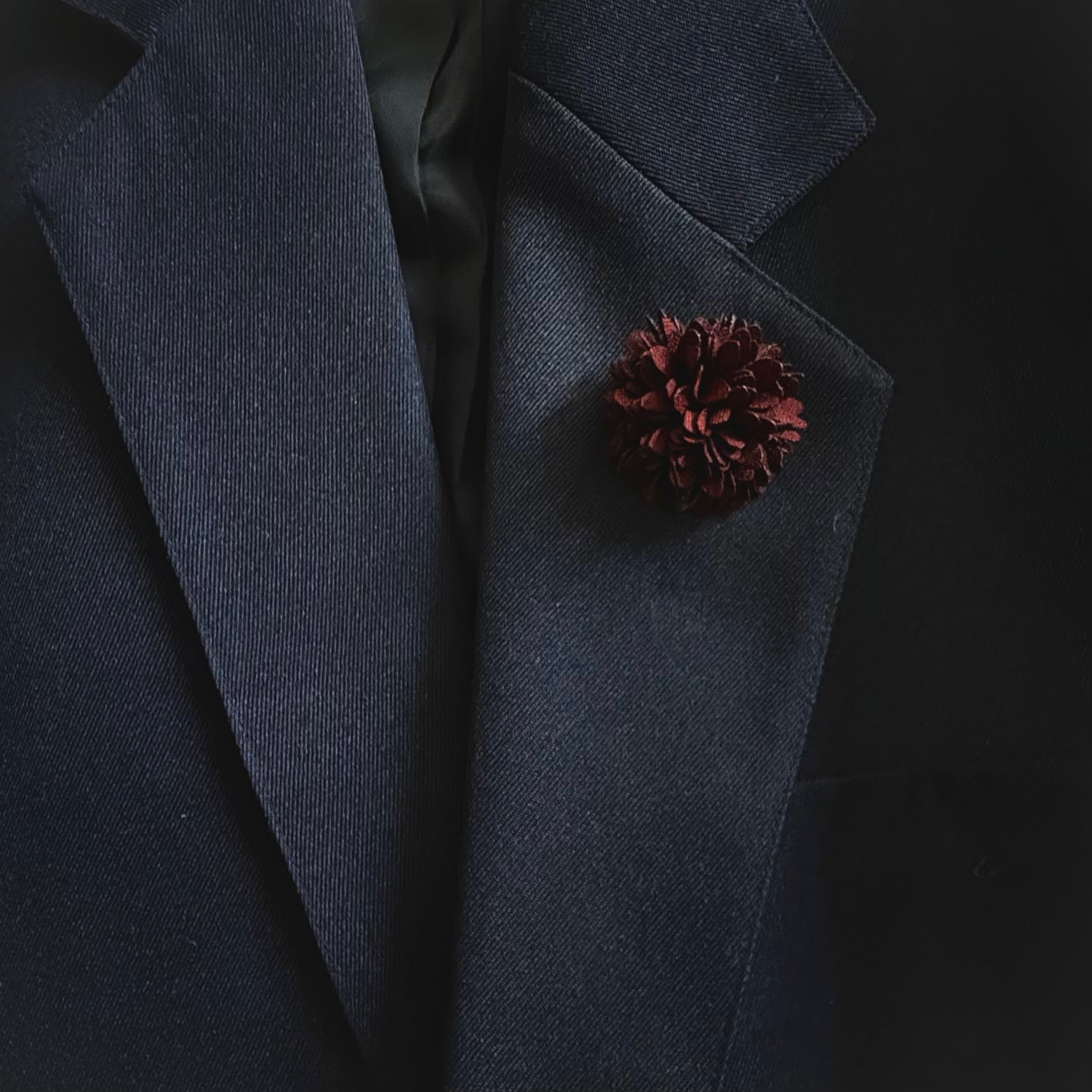 Dark blue blazer with a pine cone-shaped pin on a black background