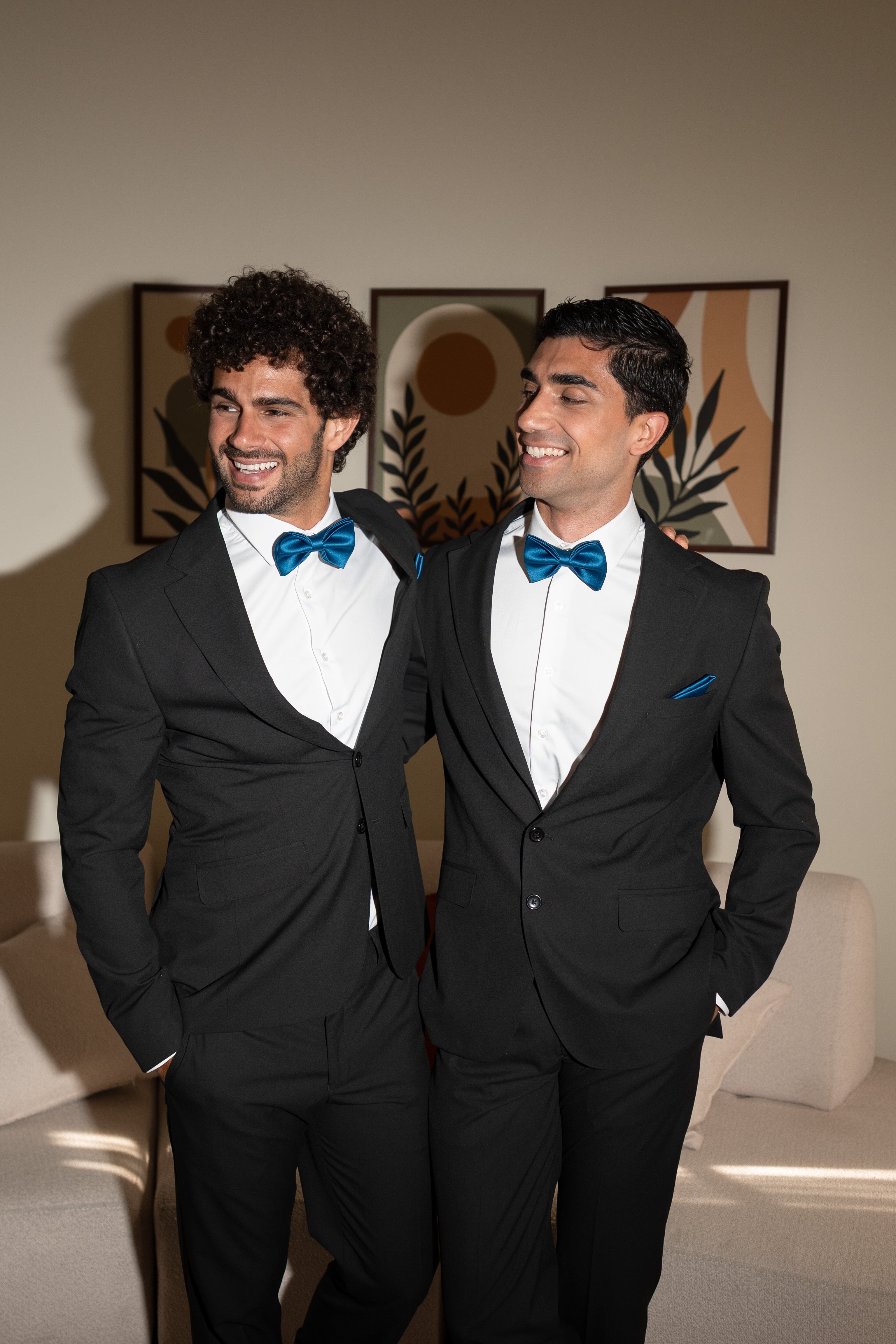 Two men in formal suits with blue bow ties standing side by side.