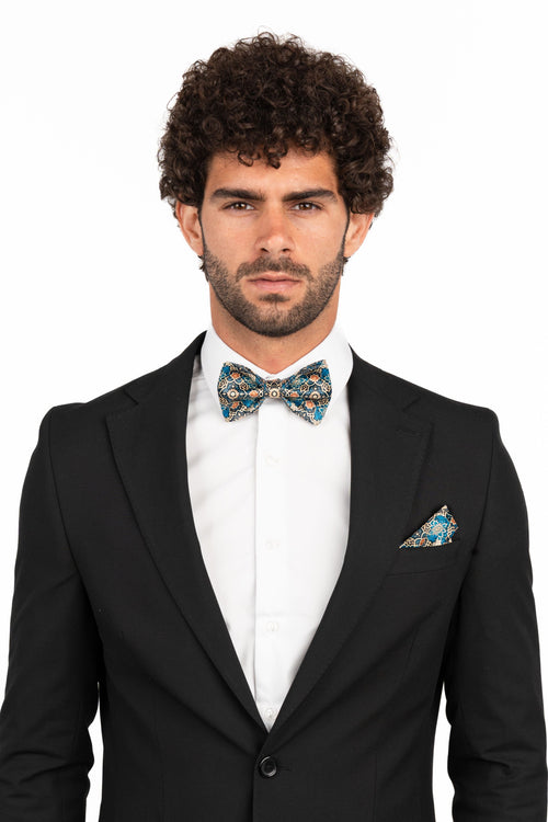 Man wearing a black suit with a patterned bow tie and pocket square on a white background