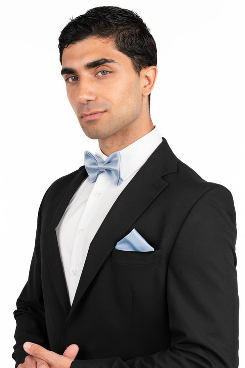 Man wearing a black tuxedo with a white shirt and light blue bow tie on a white background