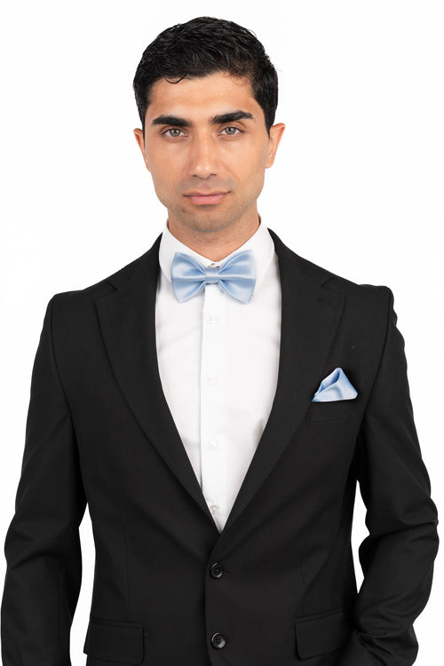 Man wearing a black suit with a light blue bow tie and pocket square on a white background