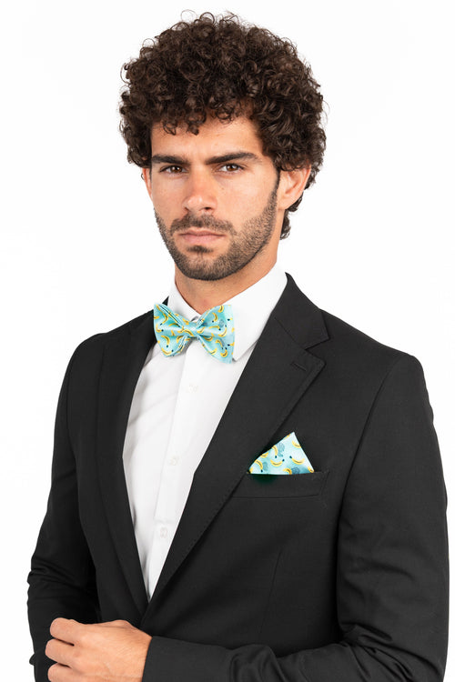 Man wearing a black suit with a white shirt and green bow tie and pocket square on a white background