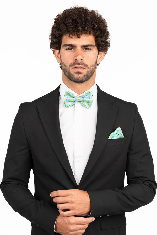 Man wearing a black suit with a white shirt and green bow tie and pocket square on a white background