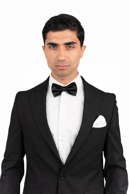 Man wearing a black tuxedo with a bow tie on a white background