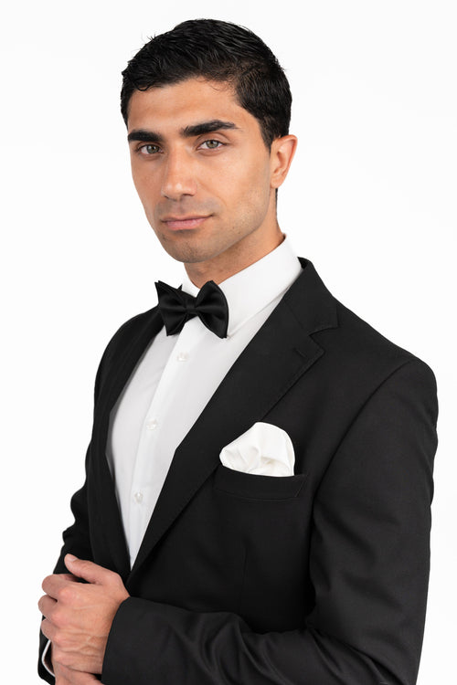 Man wearing a black tuxedo with a bow tie on a white background