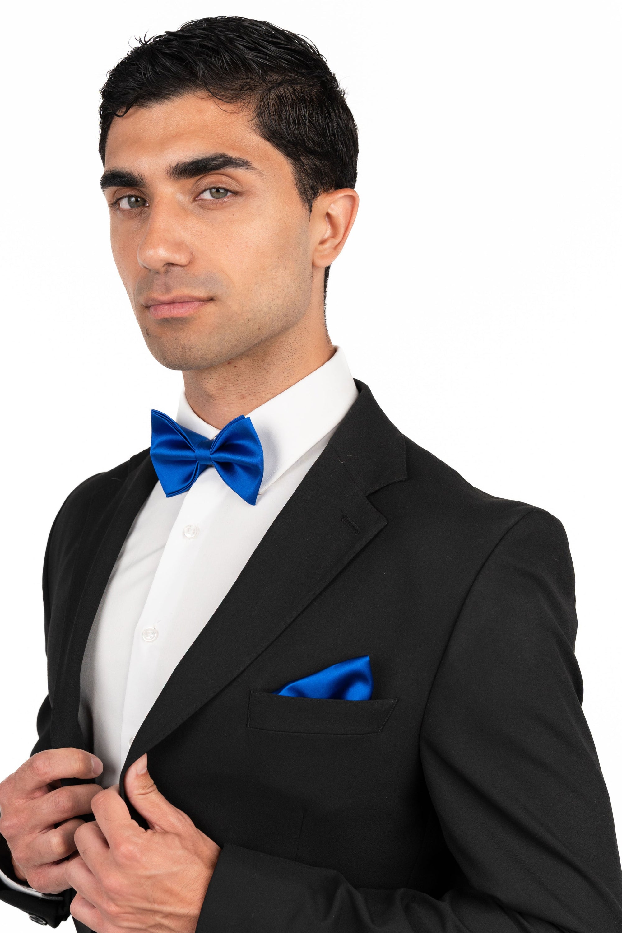 Man wearing a black tuxedo with a blue bow tie and pocket square on a white background