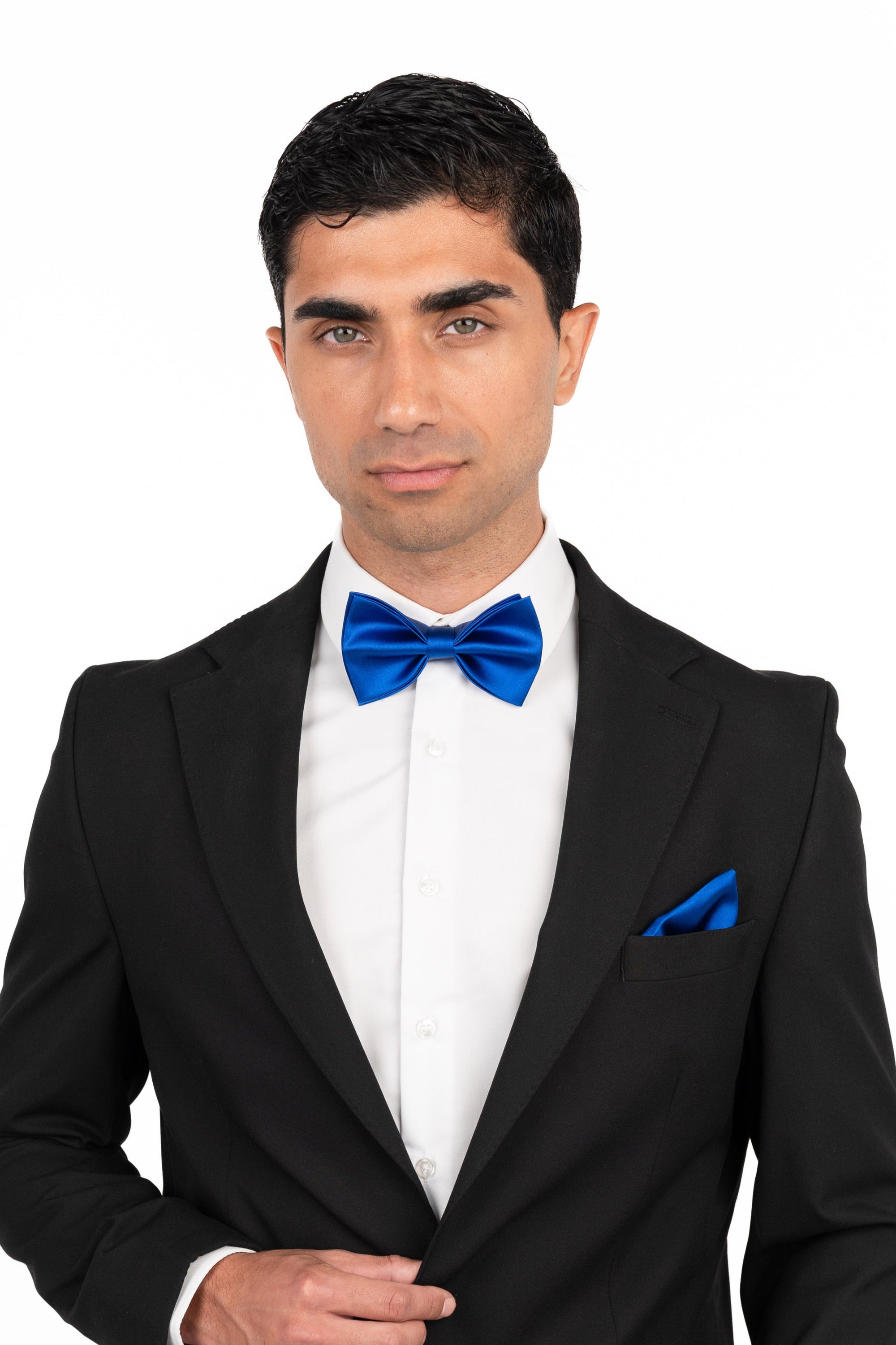 Man wearing a black tuxedo with a blue bow tie and pocket square on a white background