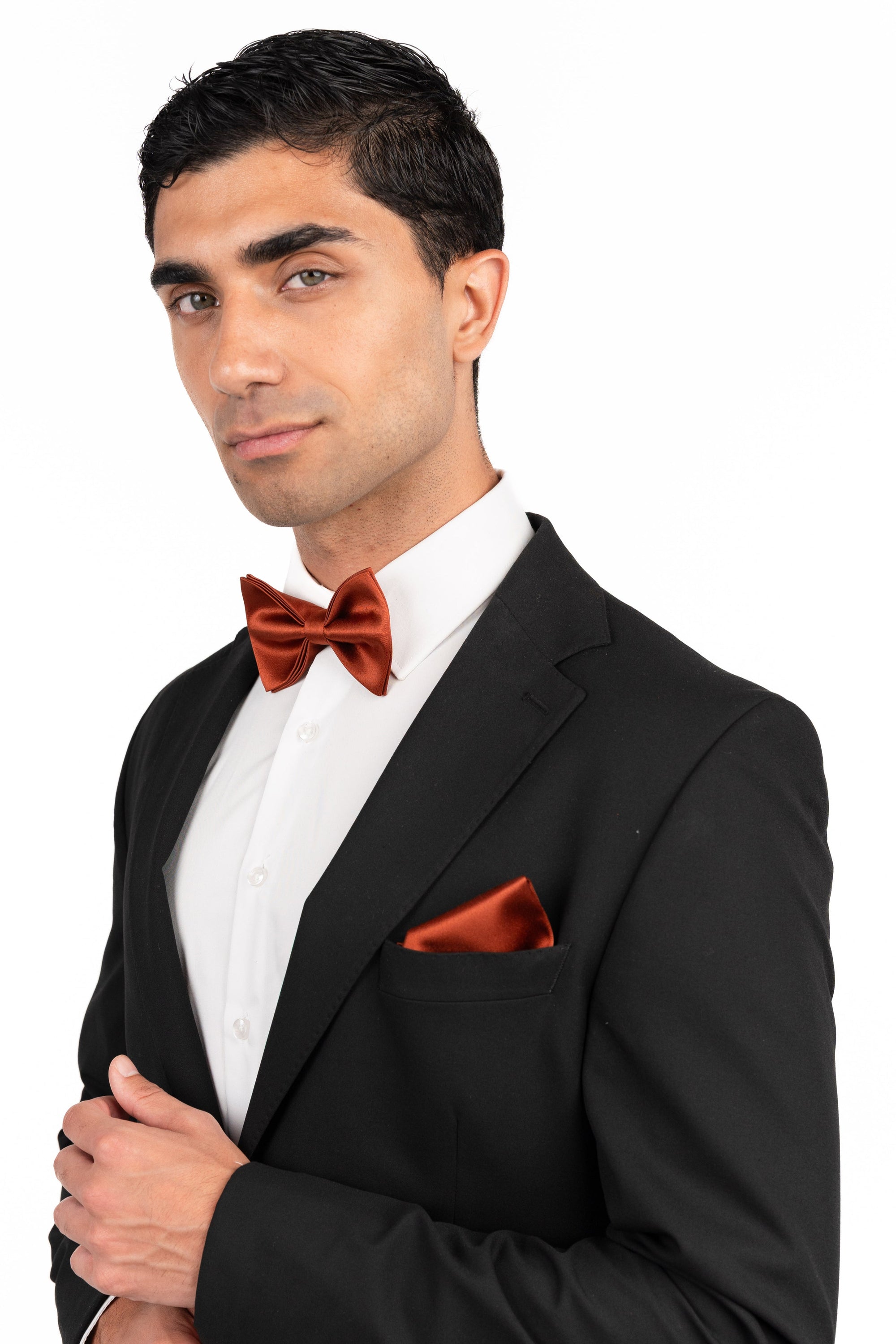Man wearing a black tuxedo with a red bow tie and pocket square on a white background