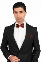 Man wearing a black tuxedo with a red bow tie and pocket square on a white background