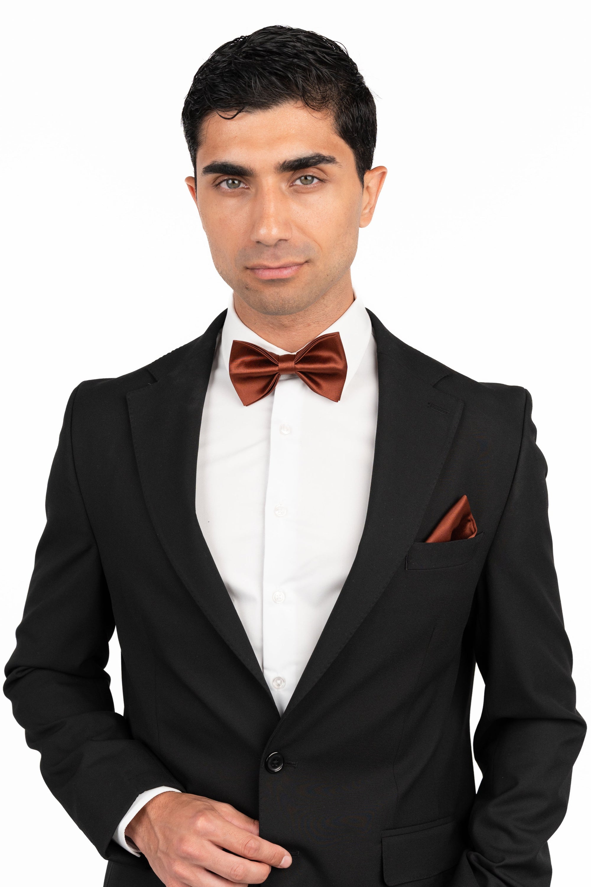 Man wearing a black tuxedo with a red bow tie and pocket square on a white background