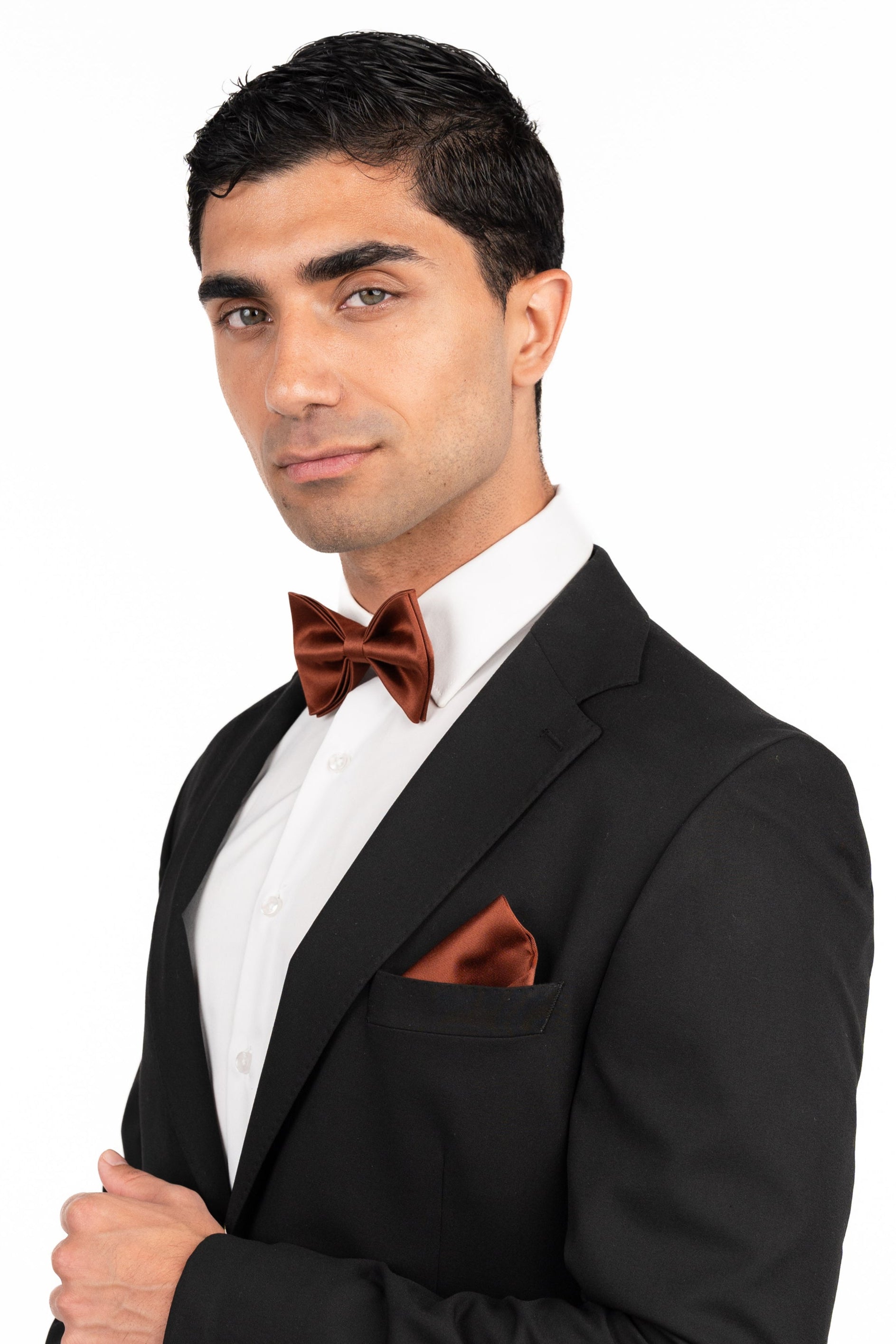 Man wearing a black tuxedo with a red bow tie and pocket square on a white background