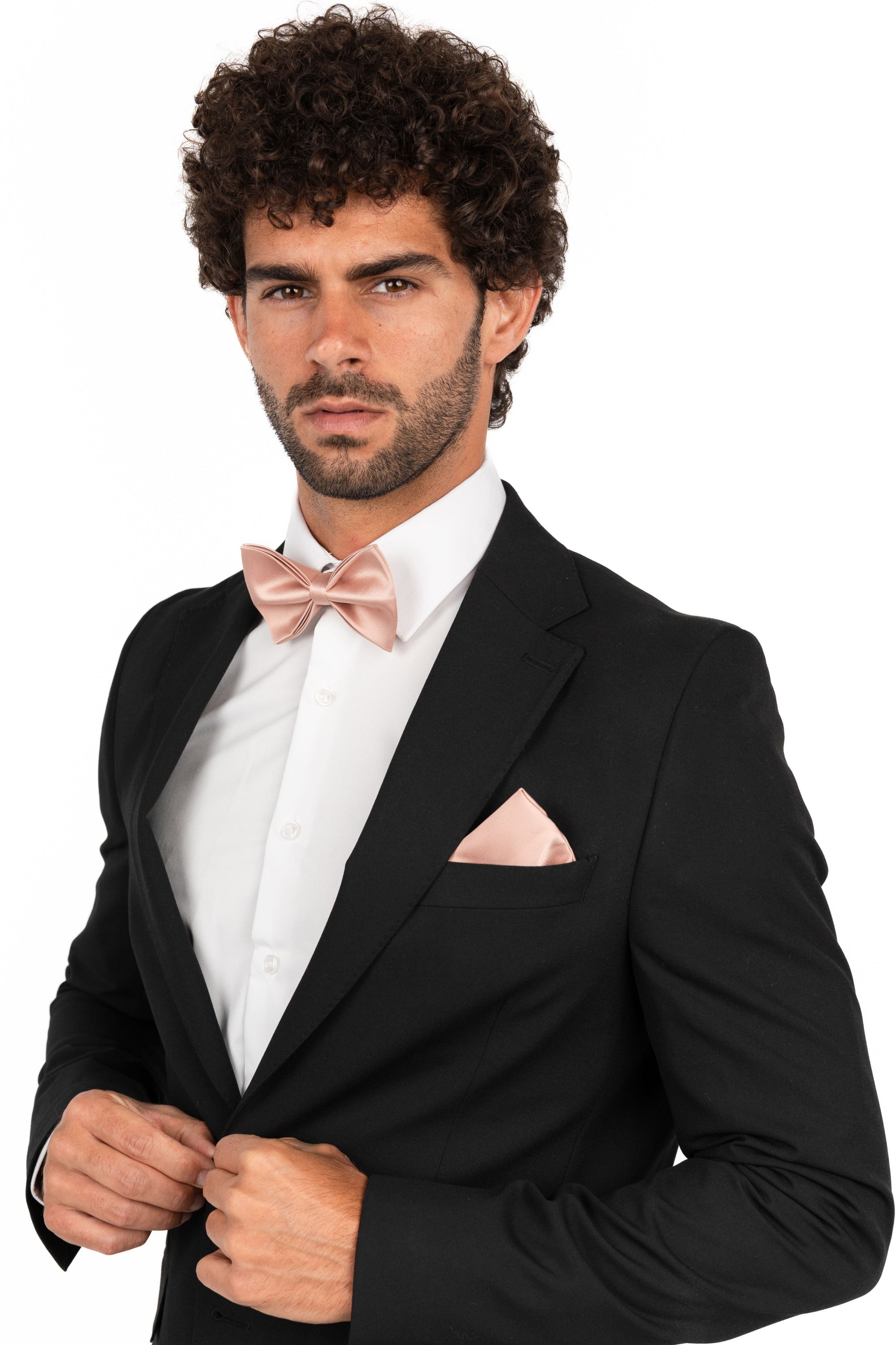 Man wearing a black tuxedo with a white shirt and pink bow tie on a white background