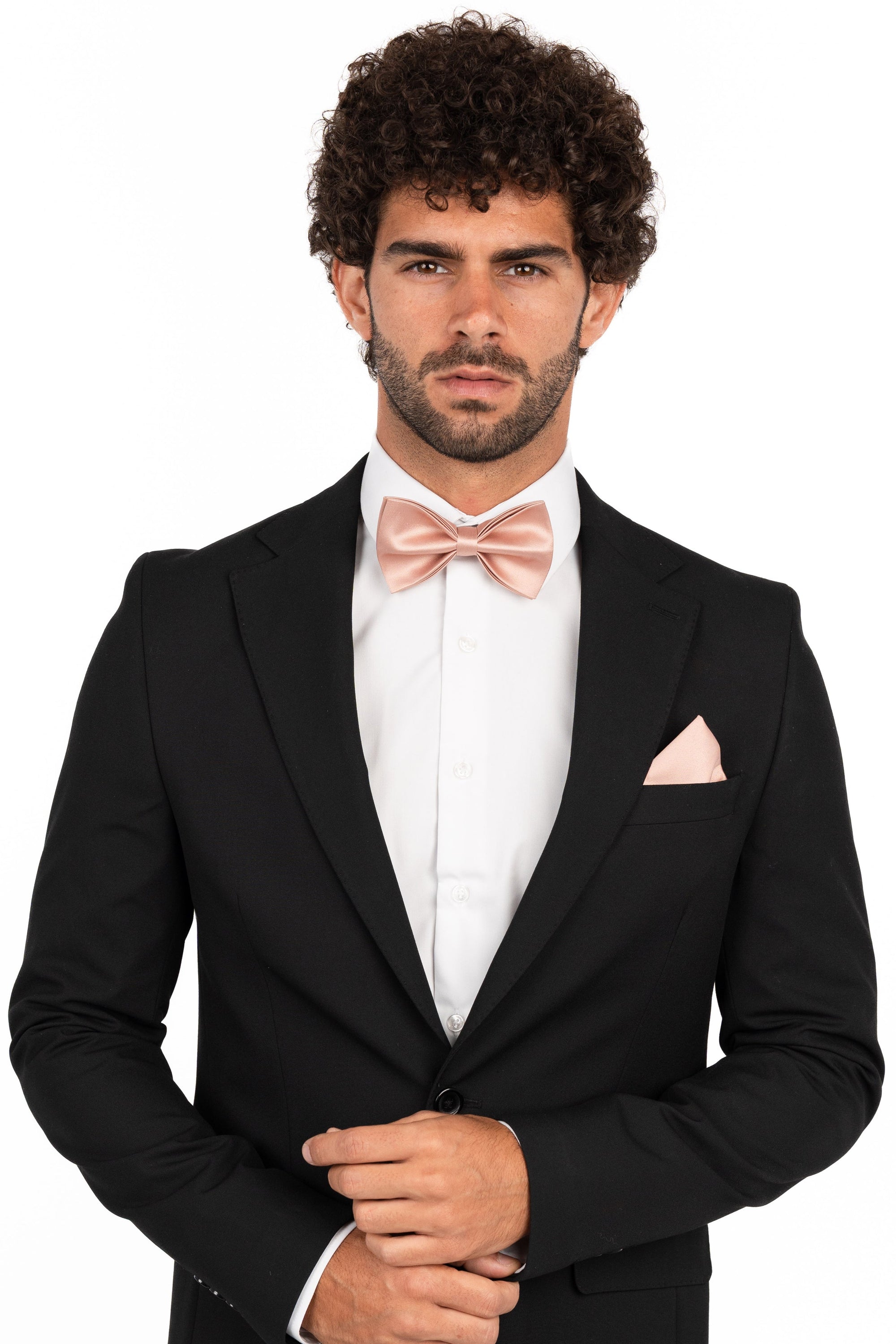 Man wearing a black tuxedo with a white shirt and pink bow tie and pocket square on a white background