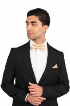 Man wearing a black tuxedo with a white shirt and gold bow tie on a white background