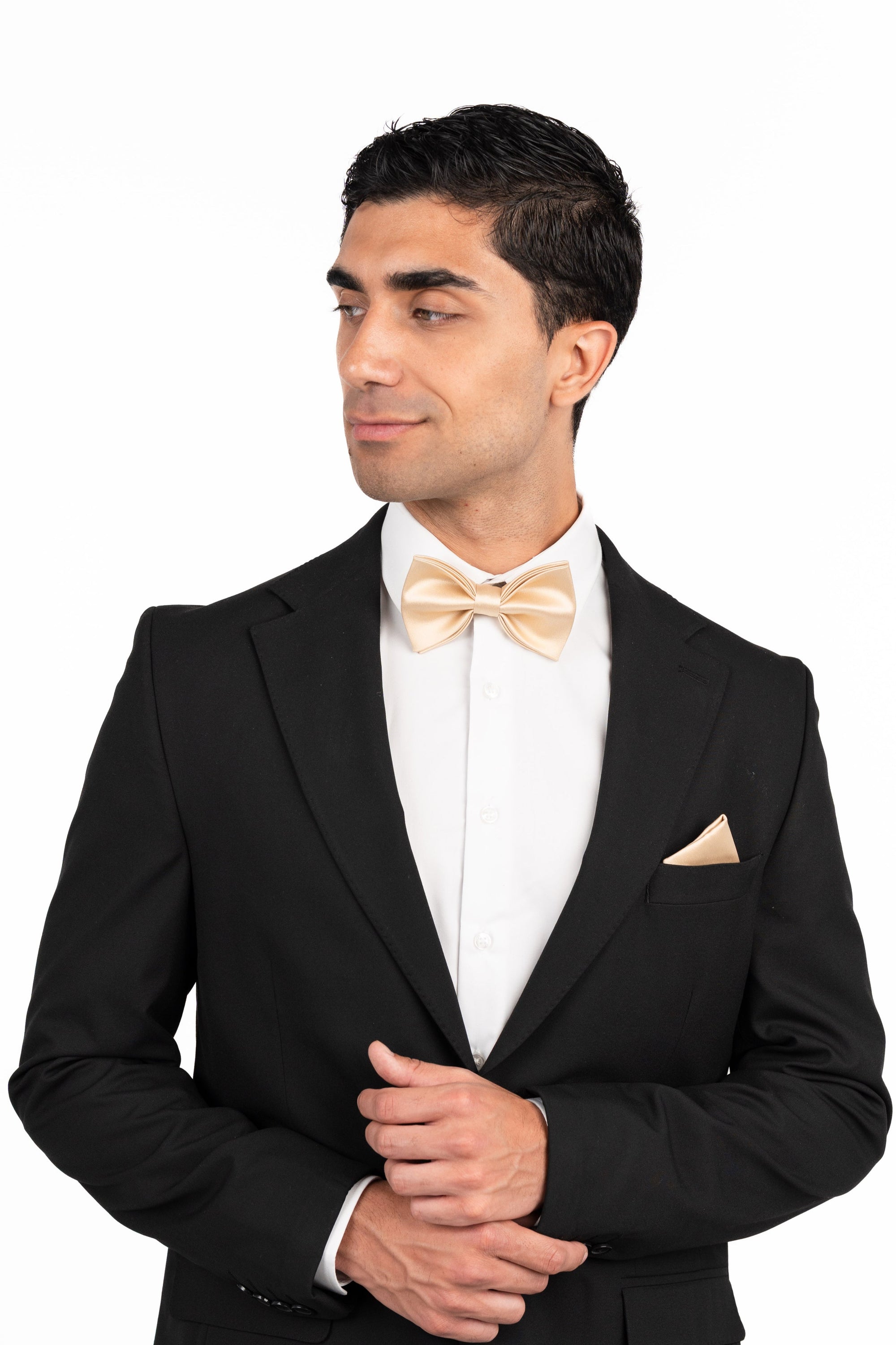 Man wearing a black tuxedo with a white shirt and gold bow tie on a white background