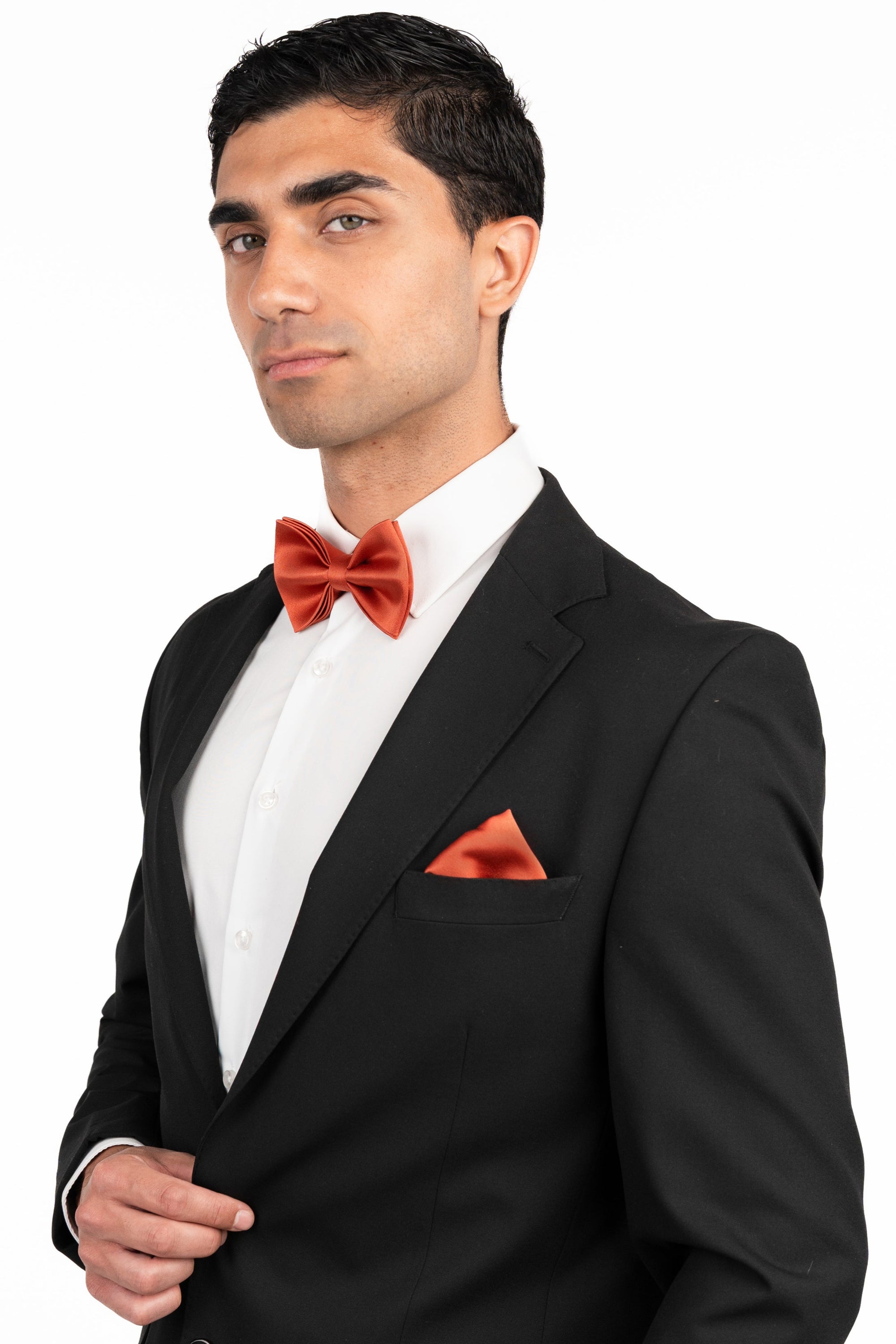 Man wearing a black suit with a red bow tie and pocket square on a white background