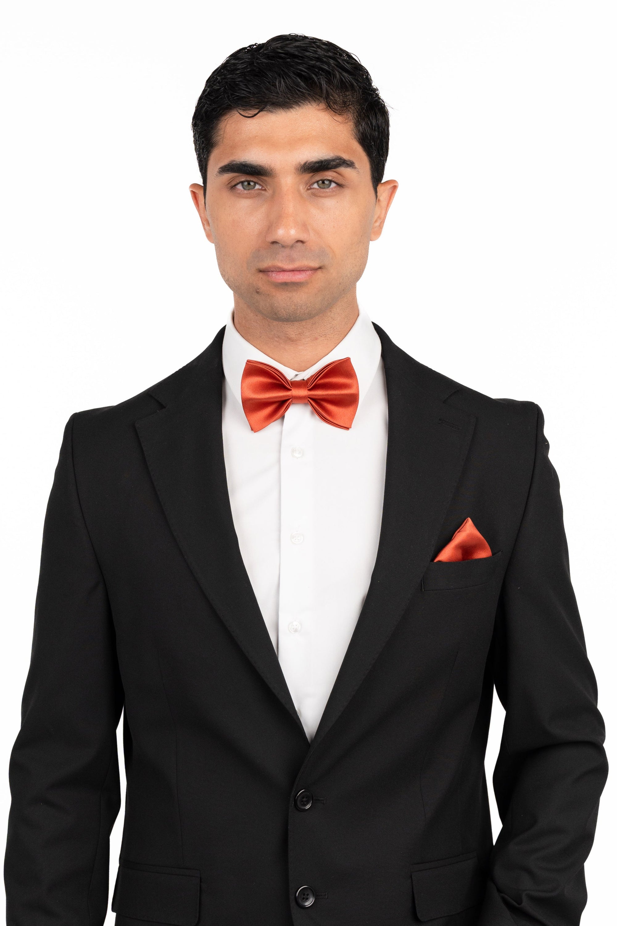 Man wearing a black suit with a red bow tie and pocket square on a white background