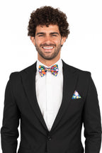 Man wearing a black suit with a colorful bow tie and pocket square on a white background