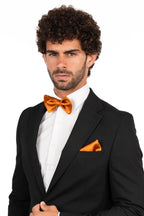 Man wearing a black suit with an orange bow tie and pocket square on a white background