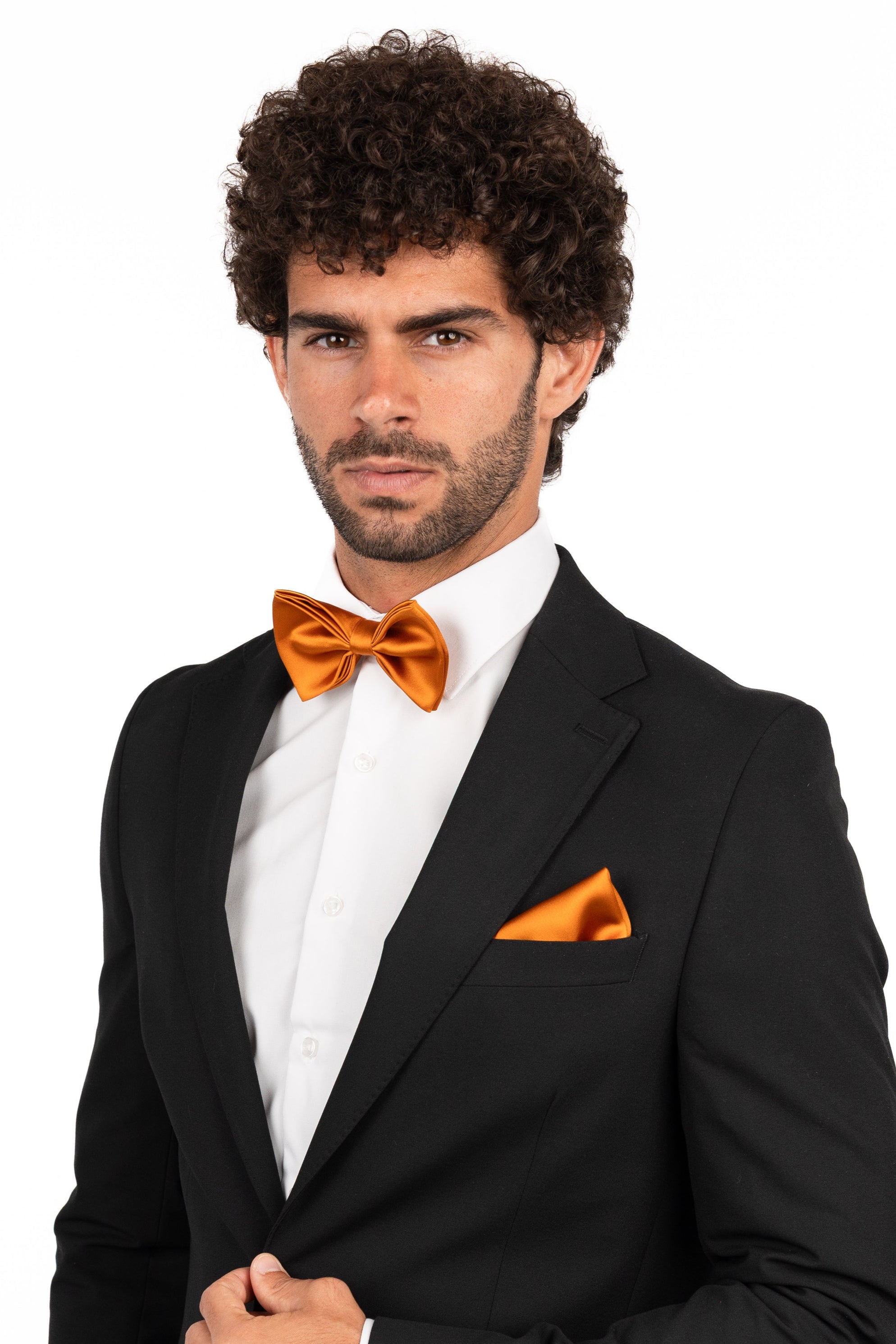 Man wearing a black suit with an orange bow tie and pocket square on a white background