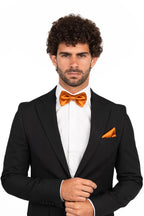 Man wearing a black suit with an orange bow tie and pocket square on a white background