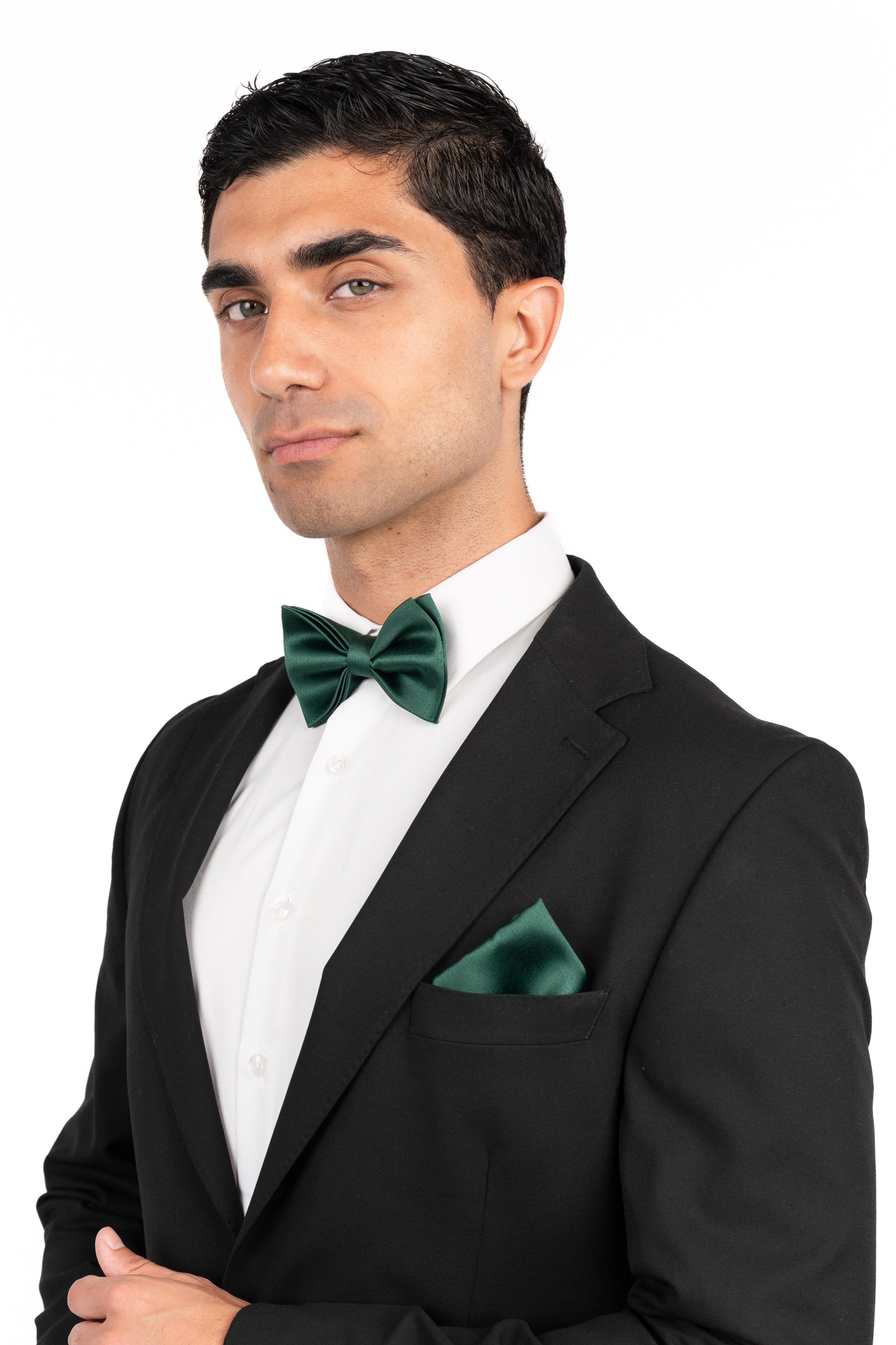 Man wearing a black tuxedo with a white shirt and green bow tie and pocket square on a white background
