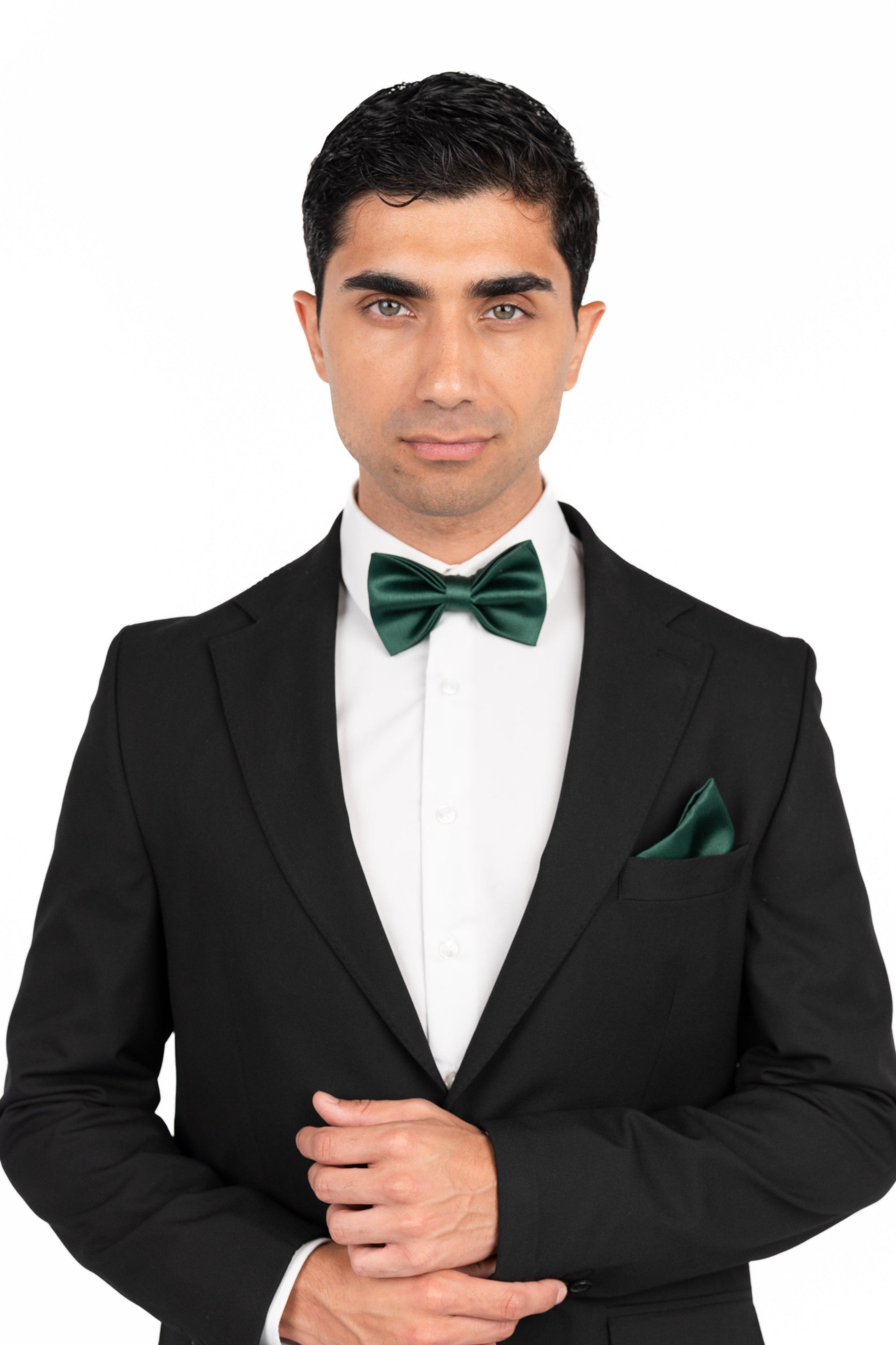 Man wearing a black tuxedo with a green bow tie and pocket square on a white background