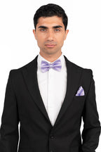 Man wearing a black suit with a white shirt and purple bow tie and pocket square on a white background