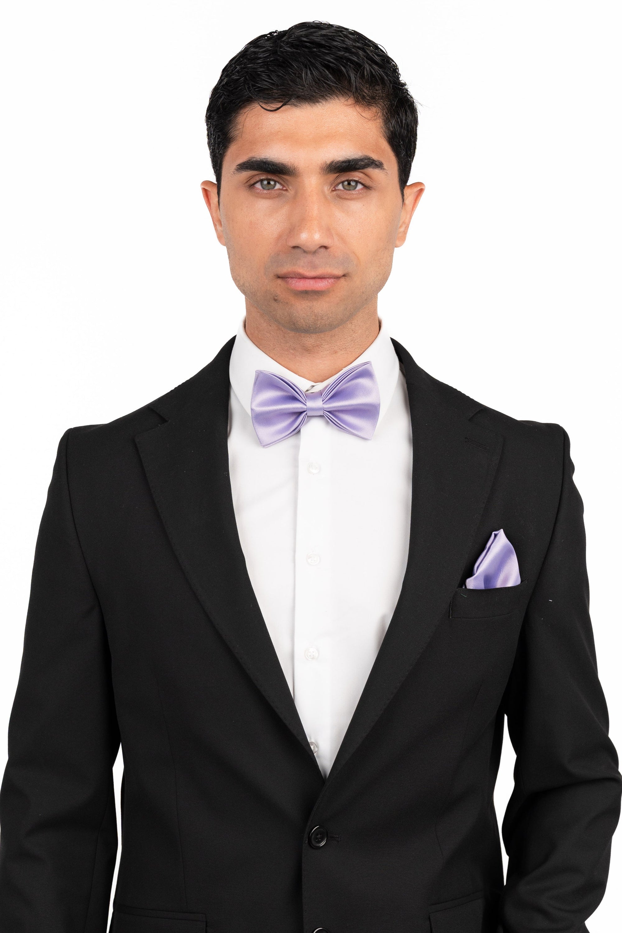 Man wearing a black suit with a white shirt and purple bow tie and pocket square on a white background