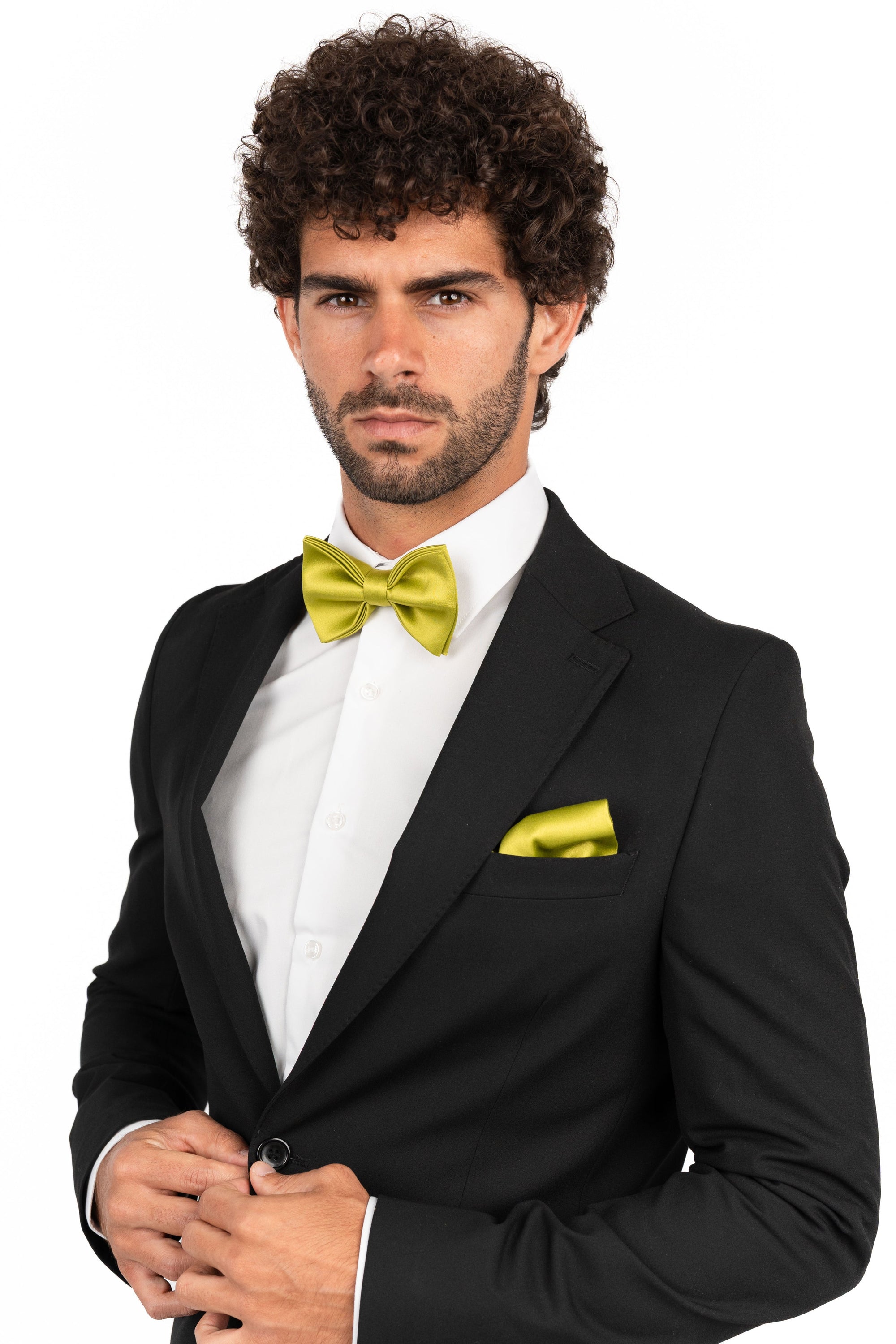 Man wearing a black tuxedo with a yellow bow tie and pocket square on a white background