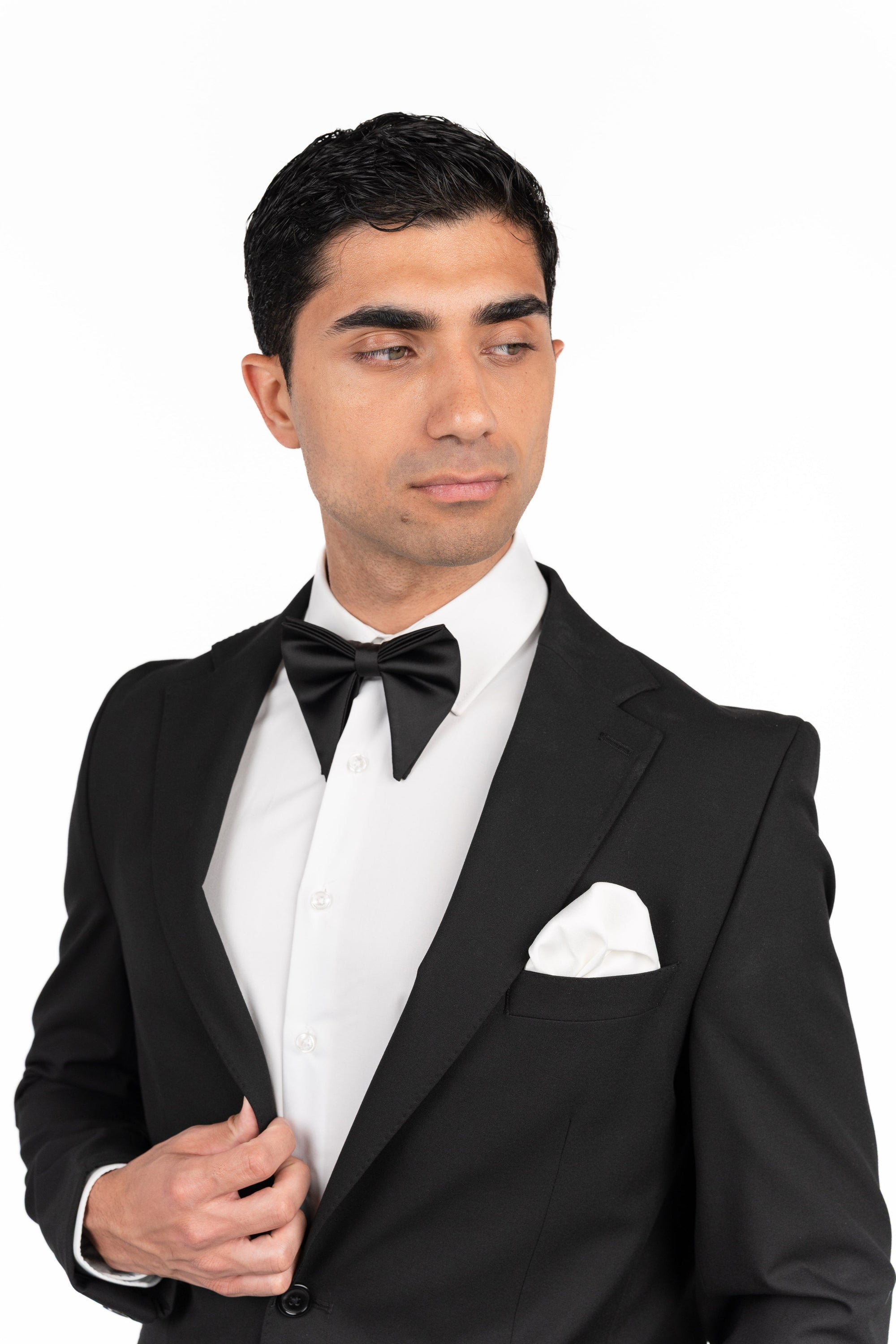 Man wearing a black tuxedo with a white shirt and bow tie on a white background