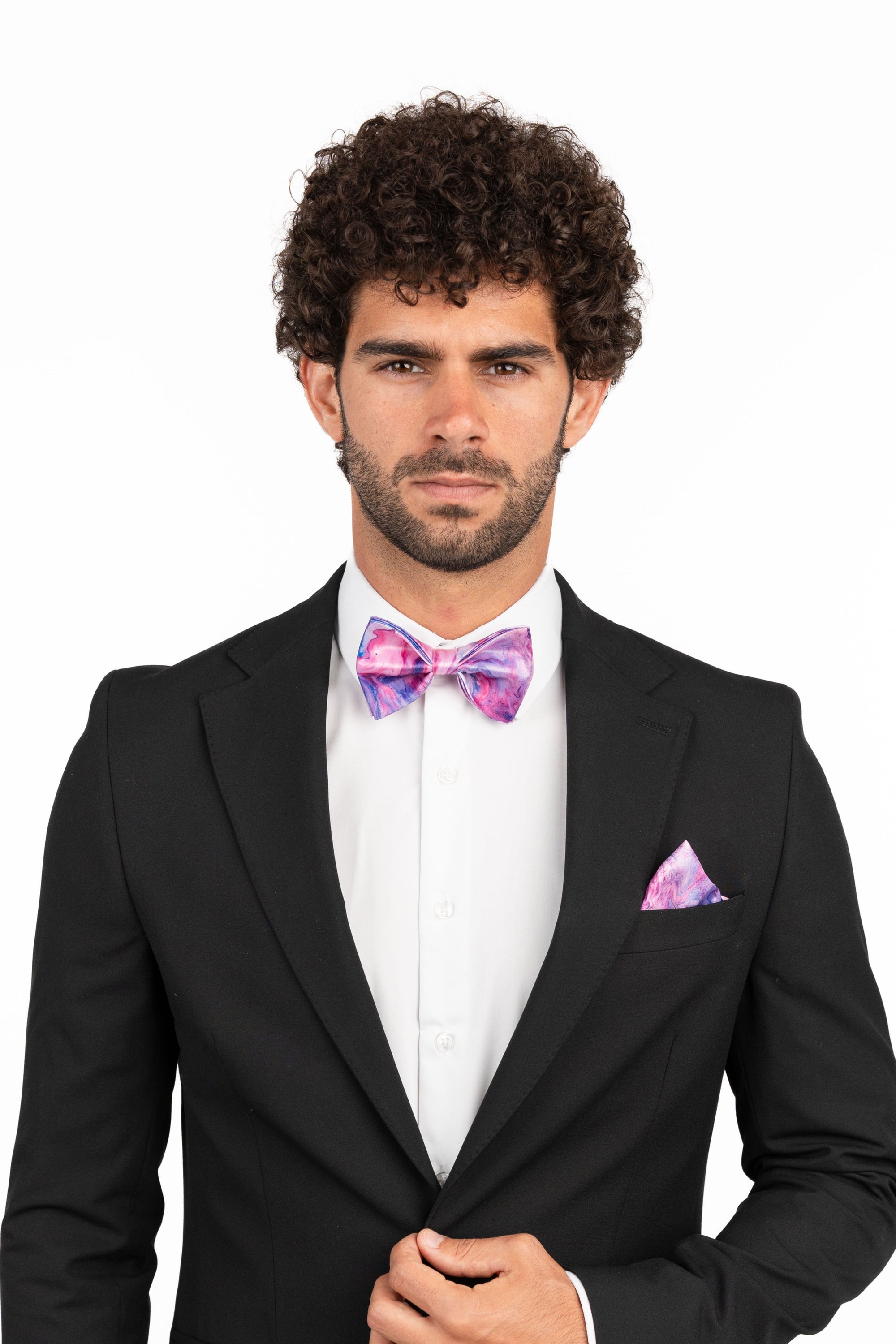 Man wearing a black suit with a white shirt, purple bow tie, and matching pocket square on a white background
