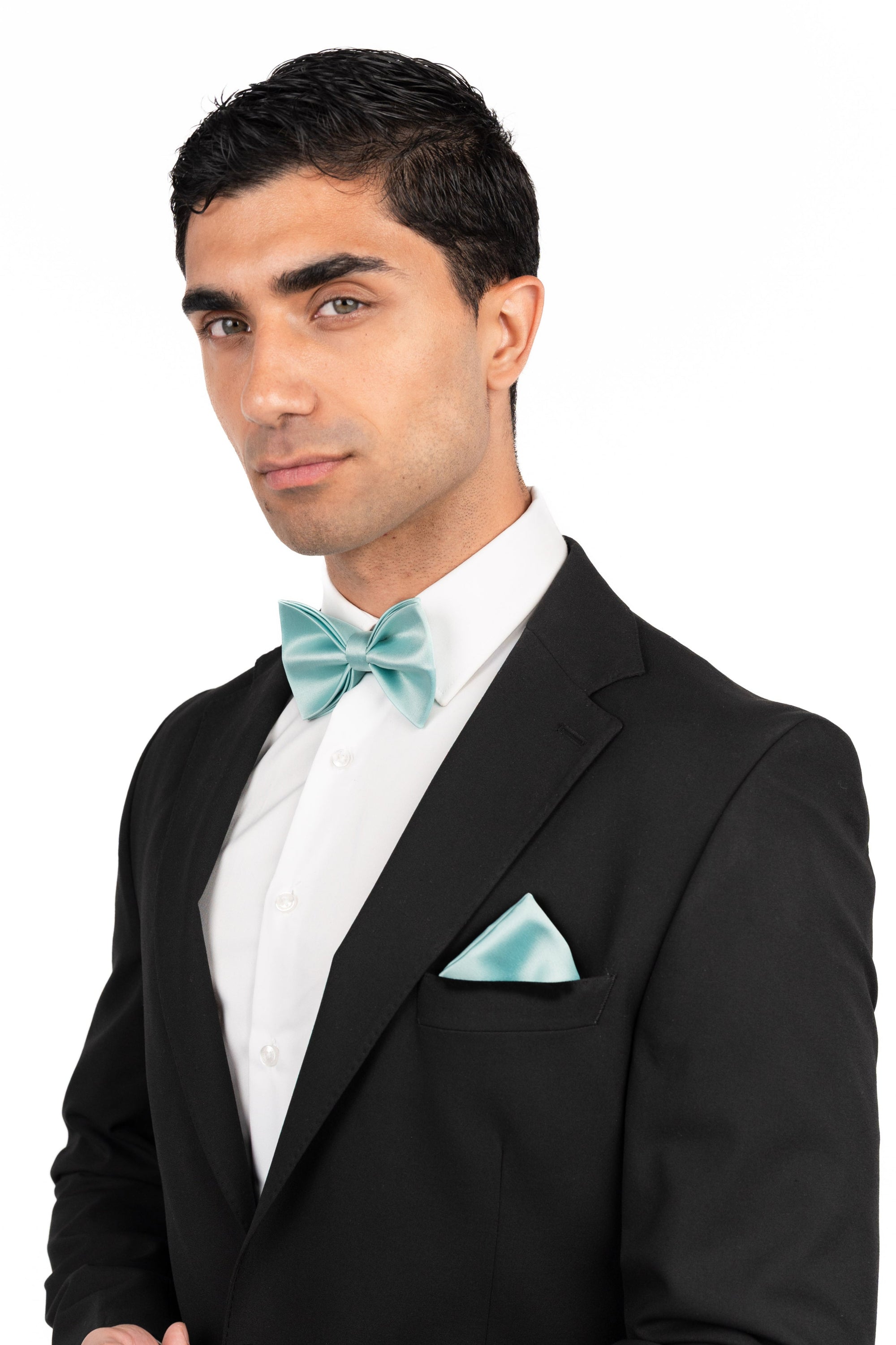 Man wearing a black tuxedo with a light blue bow tie and pocket square on a white background