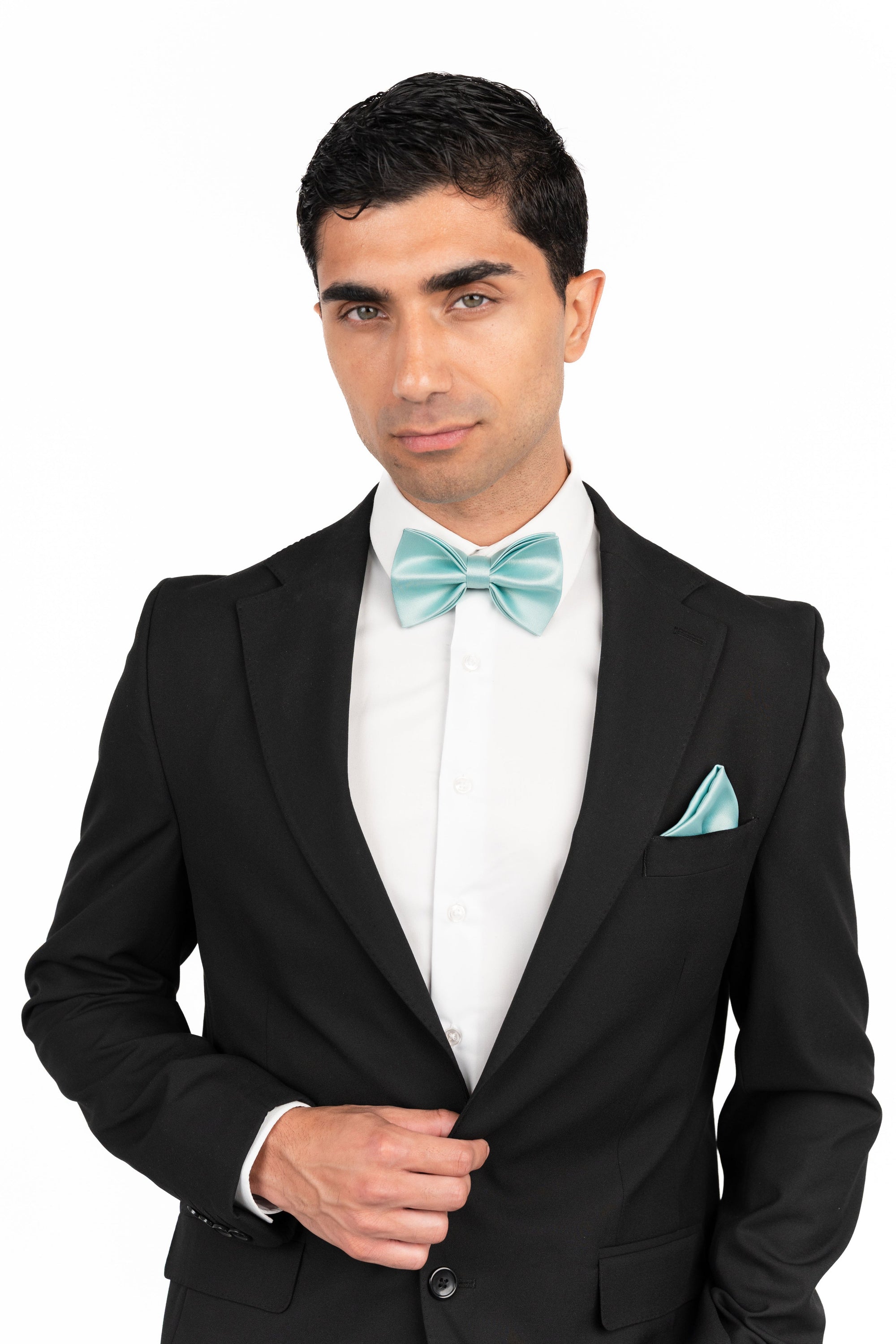 Man wearing a black suit with a white shirt and teal bow tie and pocket square on a white background