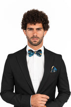 Man wearing a black suit with a colorful bow tie and pocket square on a white background
