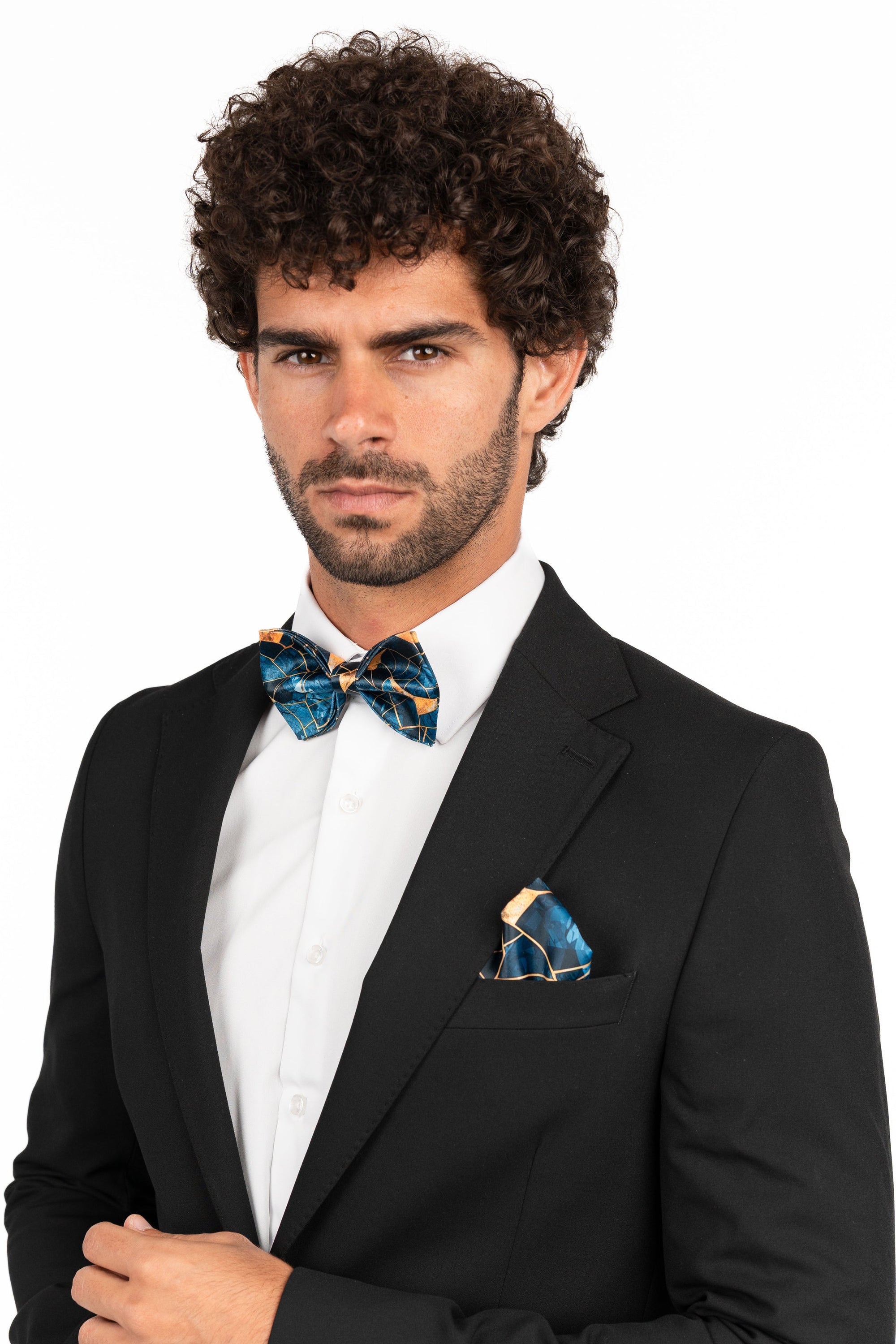 Man wearing a black suit with a white shirt and blue bow tie and pocket square on a white background