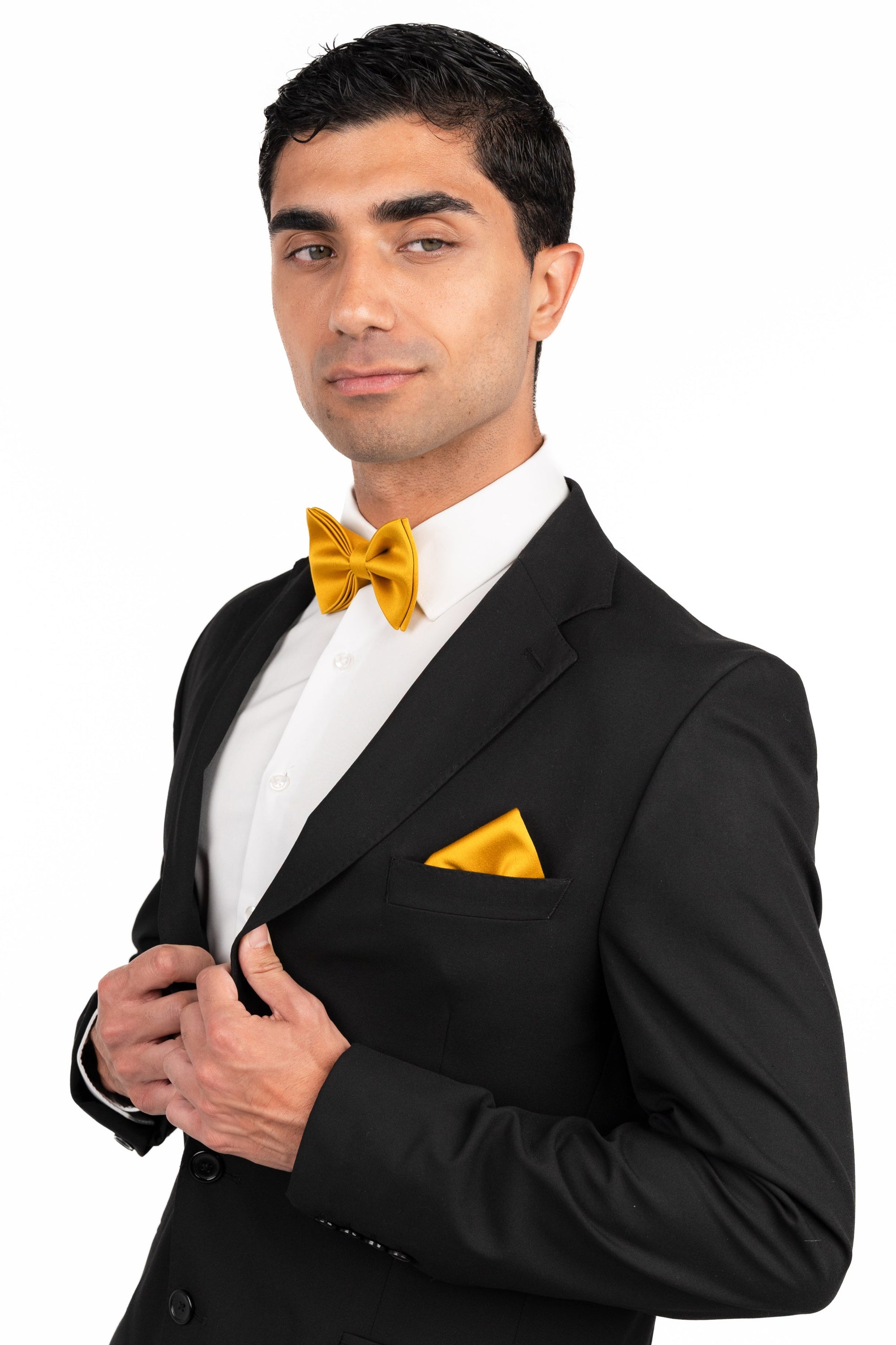 Man wearing a black tuxedo with a yellow bow tie and pocket square on a white background