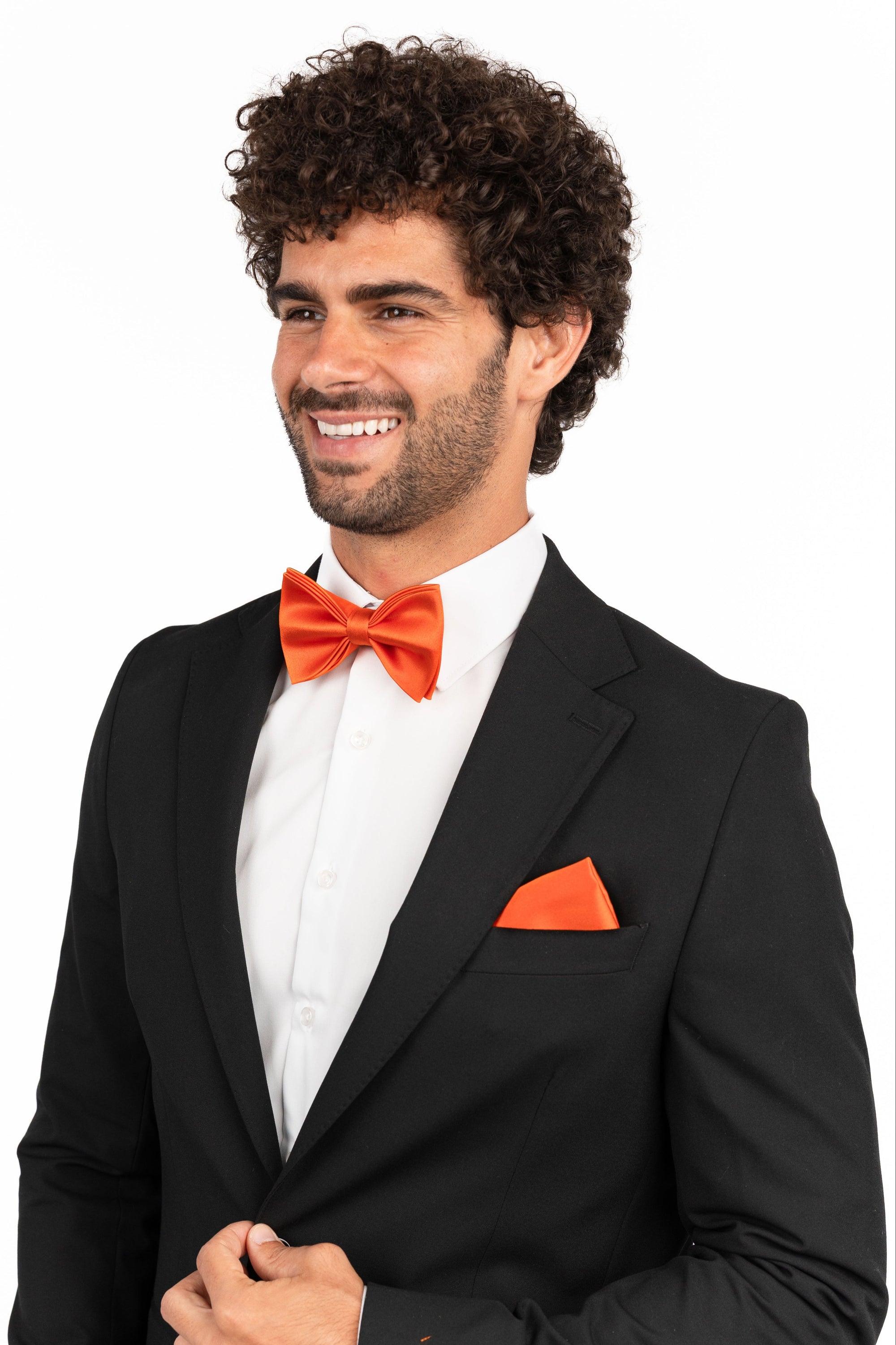 Man wearing a black tuxedo with an orange bow tie and pocket square on a white background