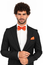 Man wearing a black suit with an orange bow tie and pocket square on a white background