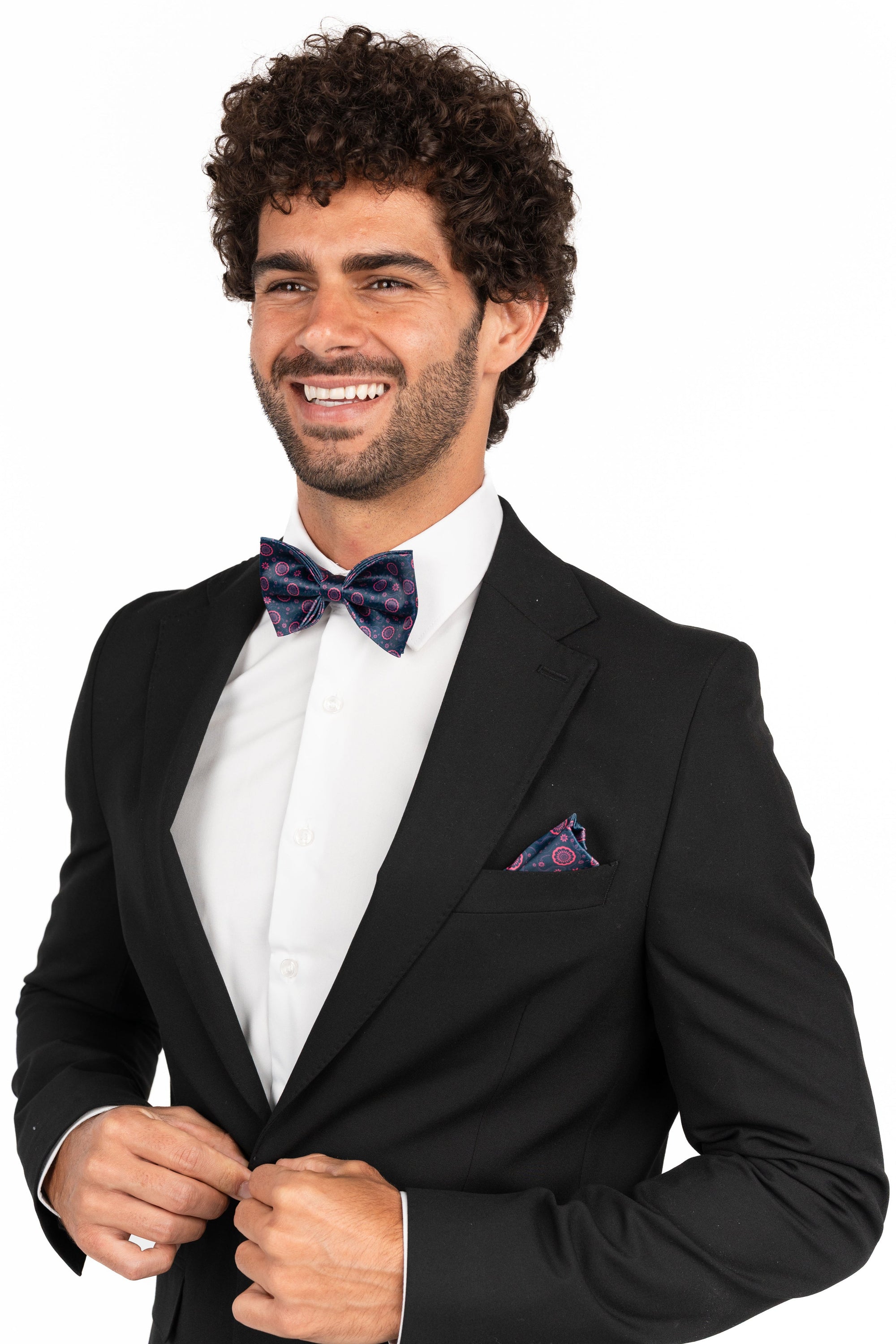 Man wearing a black tuxedo with a bow tie and pocket square on a white background