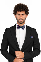 Man wearing a black tuxedo with a purple bow tie and pocket square on a white background