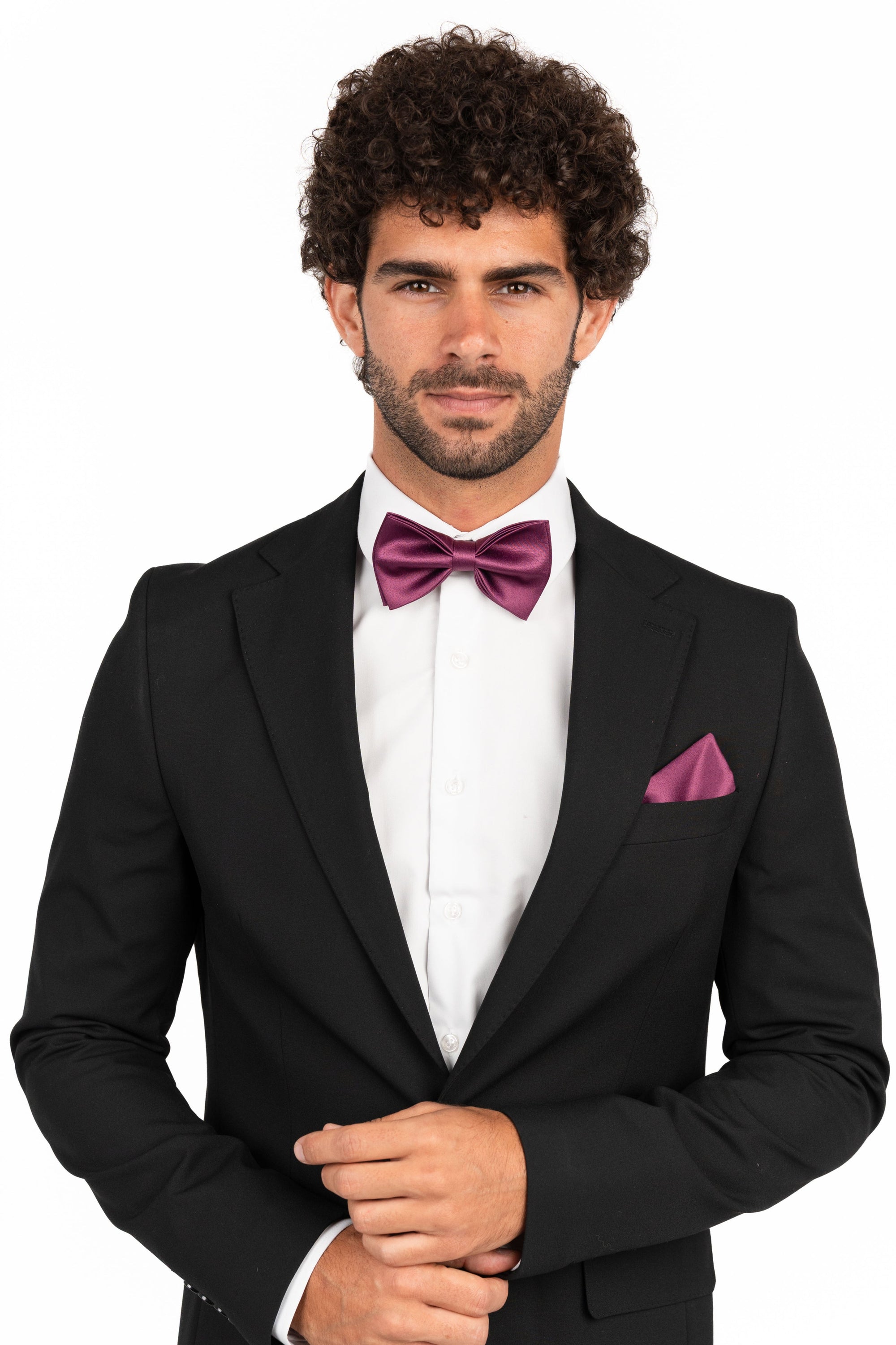 Man wearing a black suit with a white shirt and purple bow tie and pocket square on a white background