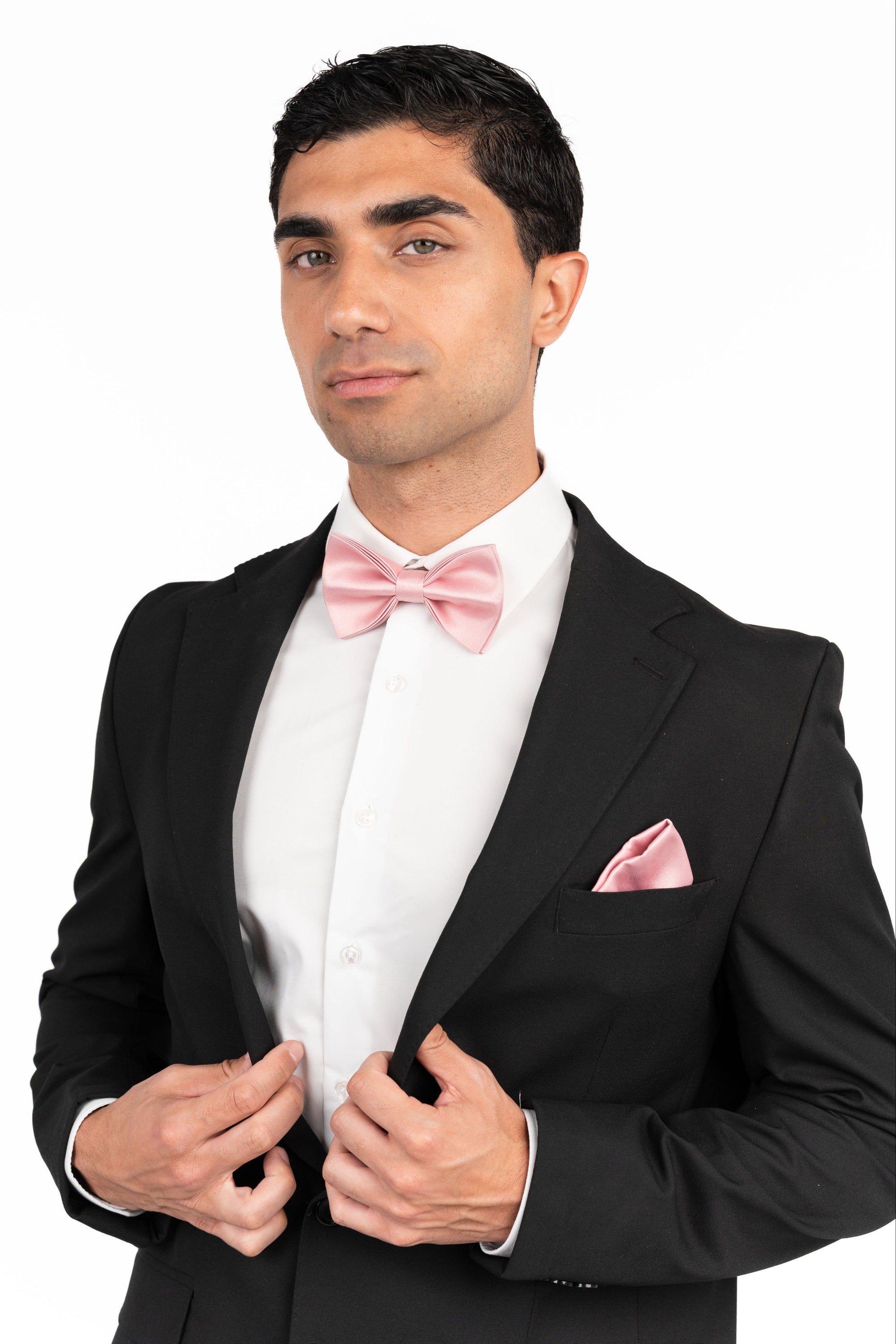 Man wearing a black tuxedo with a pink bow tie and pocket square on a white background