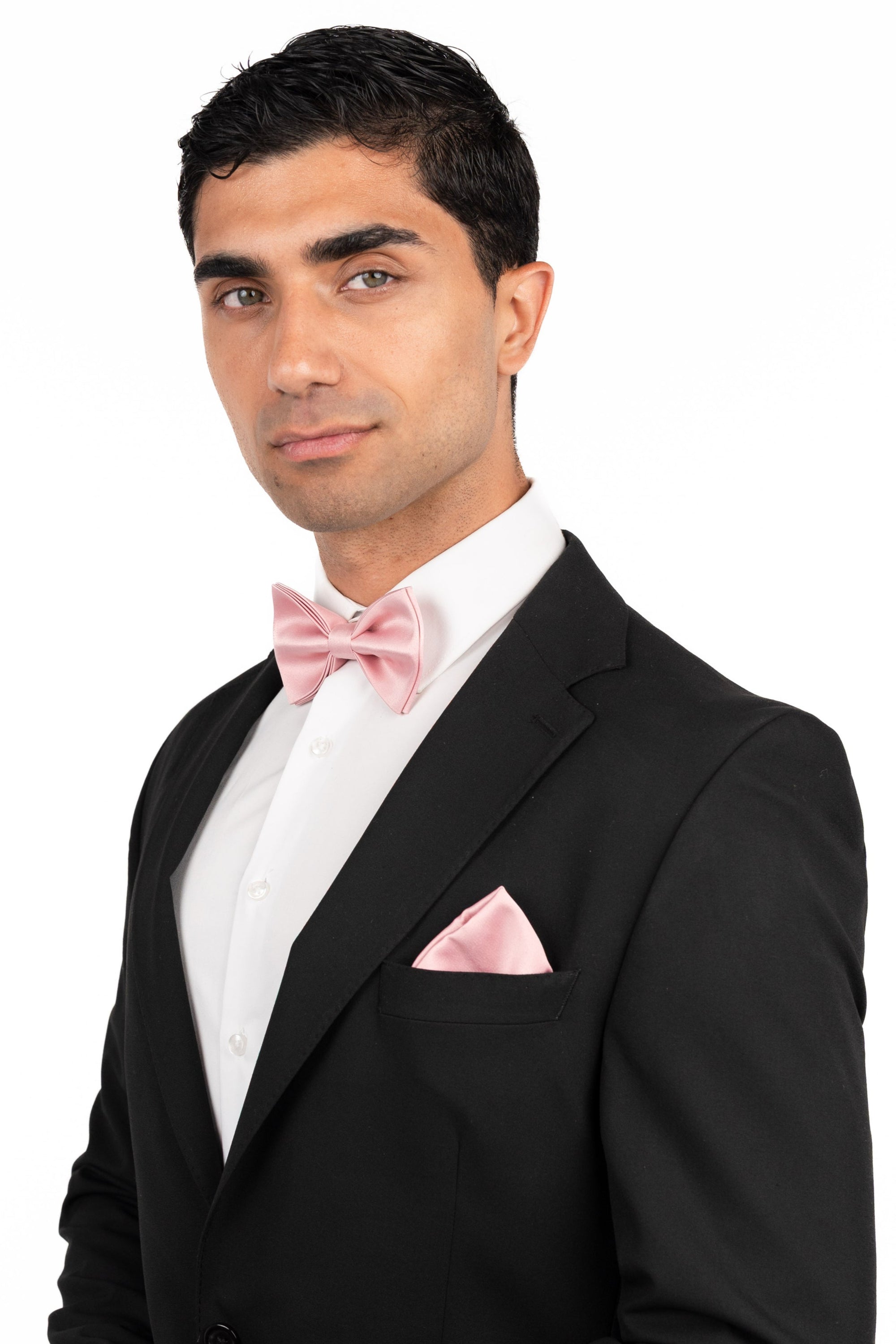 Man in a black tuxedo with a pink bow tie and pocket square on a white background
