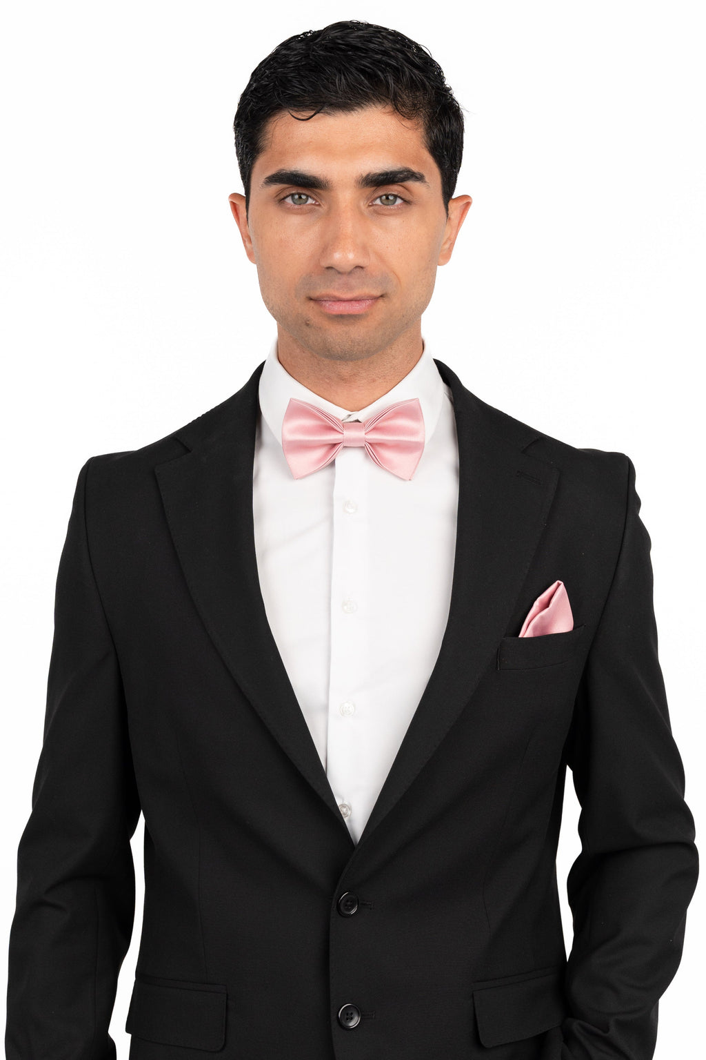 Man wearing a black suit with a white shirt and pink bow tie and pocket square on a white background